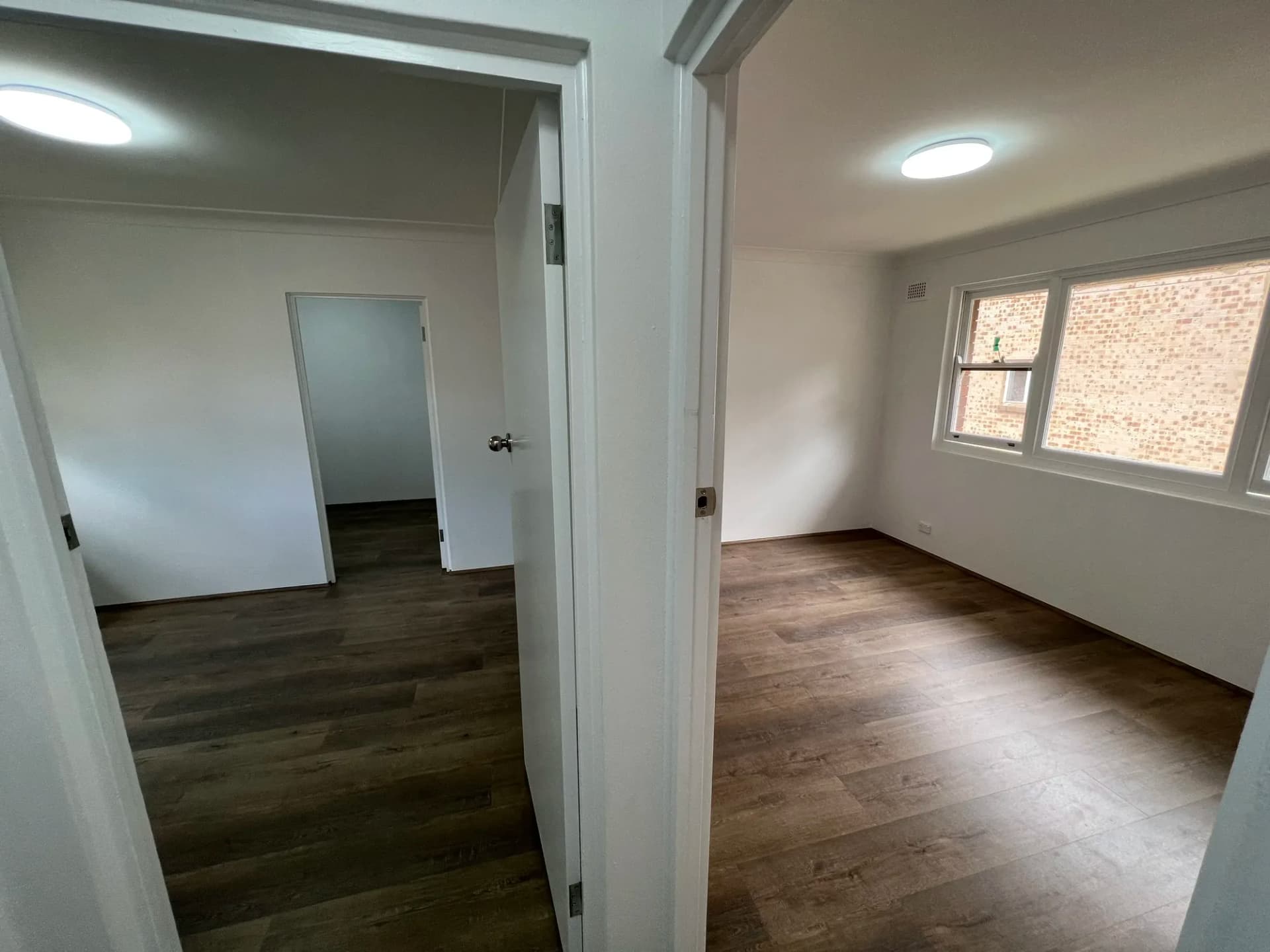 Two freshly renovated Artarmon apartment bedrooms with continuous dark timber-look flooring and white walls