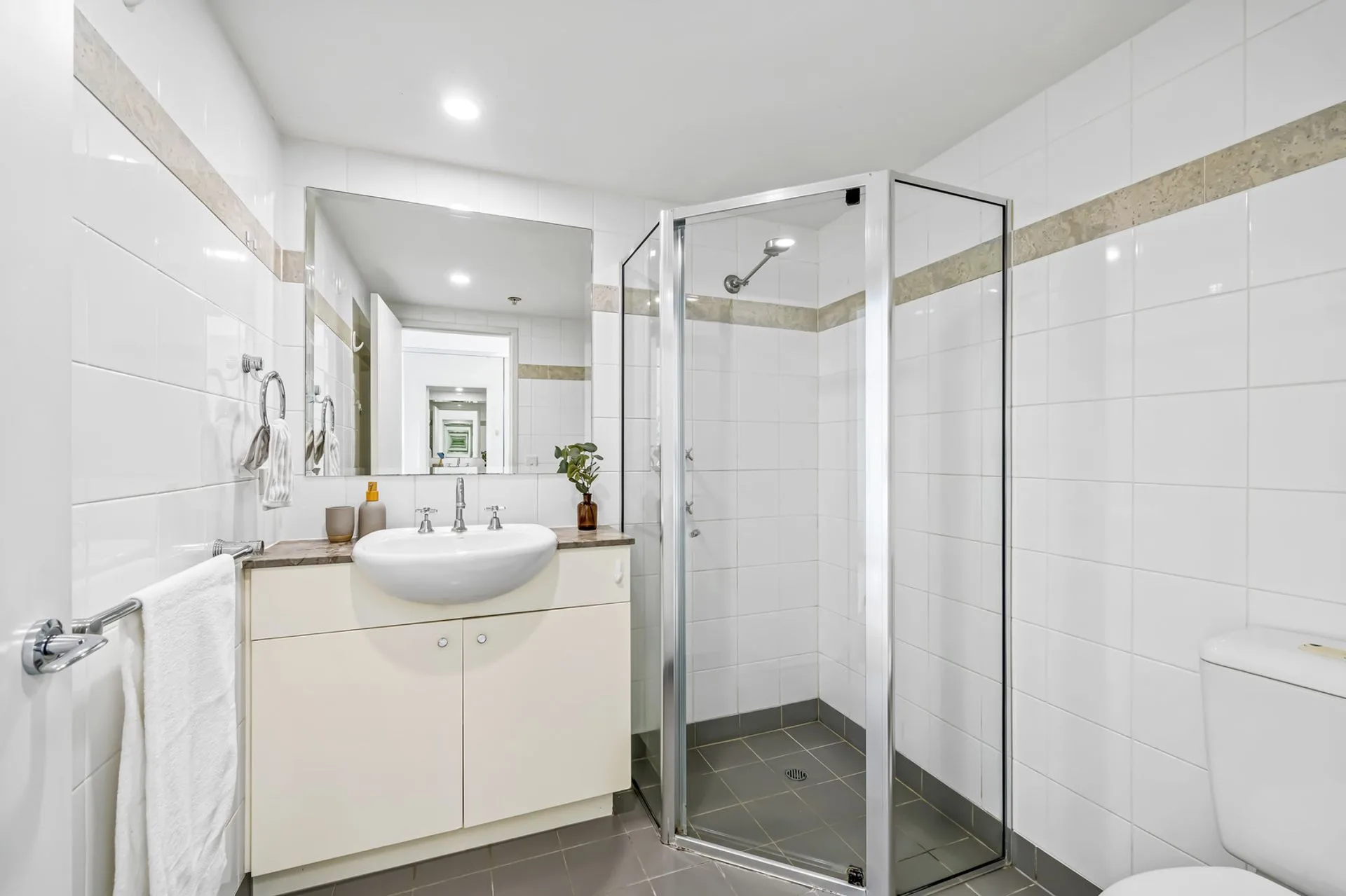 Original apartment bathroom with white square wall tiles, a cream laminate vanity and a framed corner shower