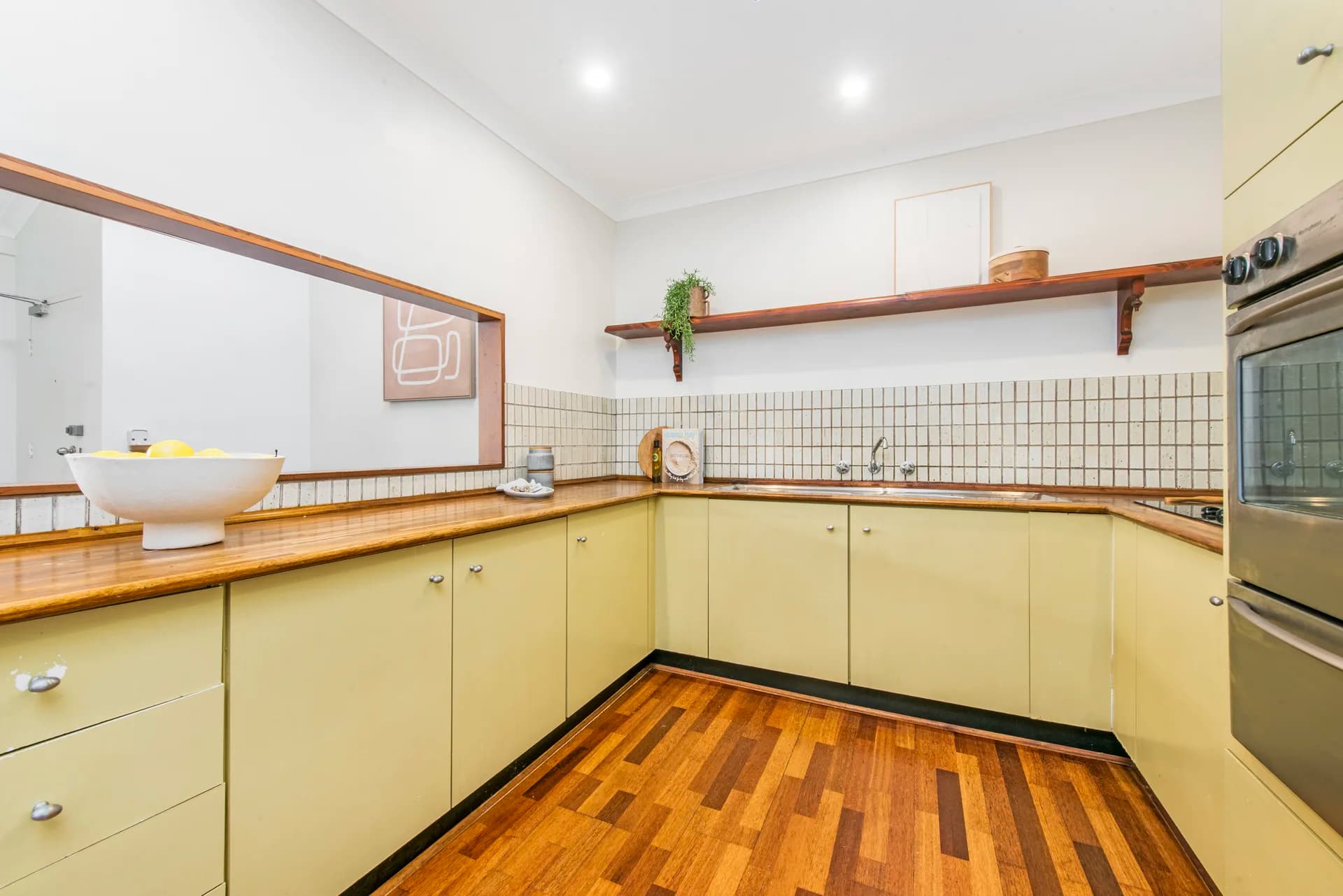Original kitchen with cream laminate doors, timber benchtop and small square tiled splashback