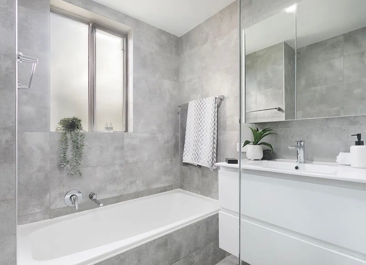Renovated apartment bathroom with grey stone tile and bathtub