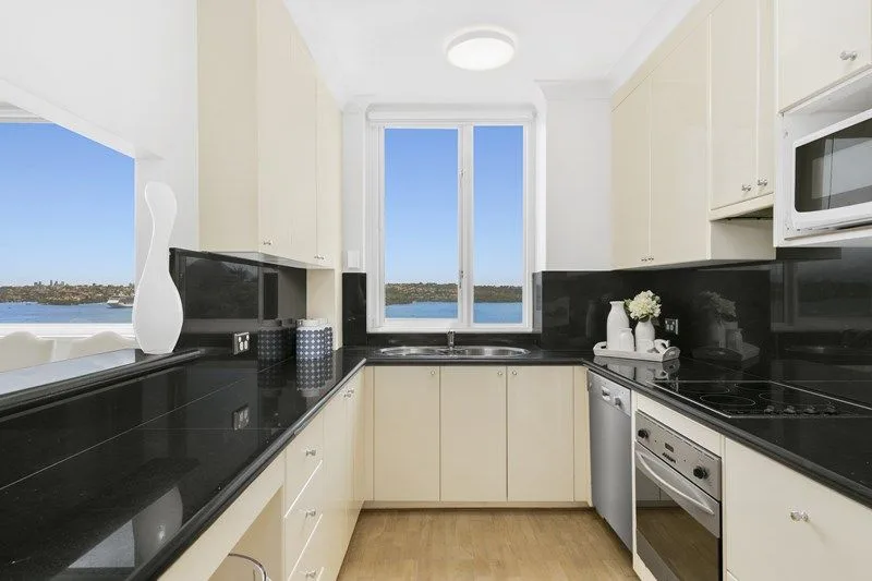 Original galley kitchen with cream doors, black benchtop and black splashback