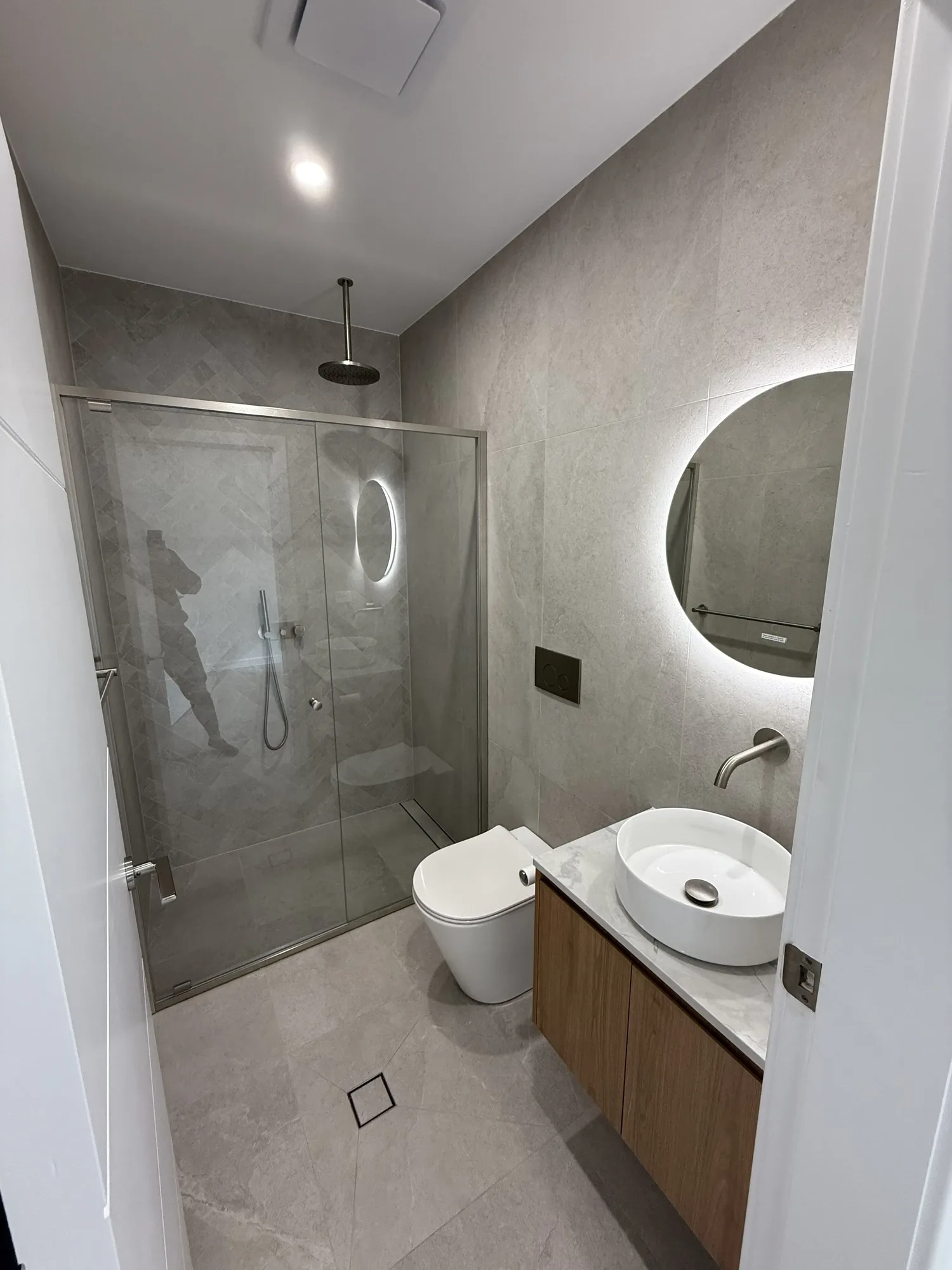 Compact renovated apartment bathroom with terrazzo floor and walk-in shower
