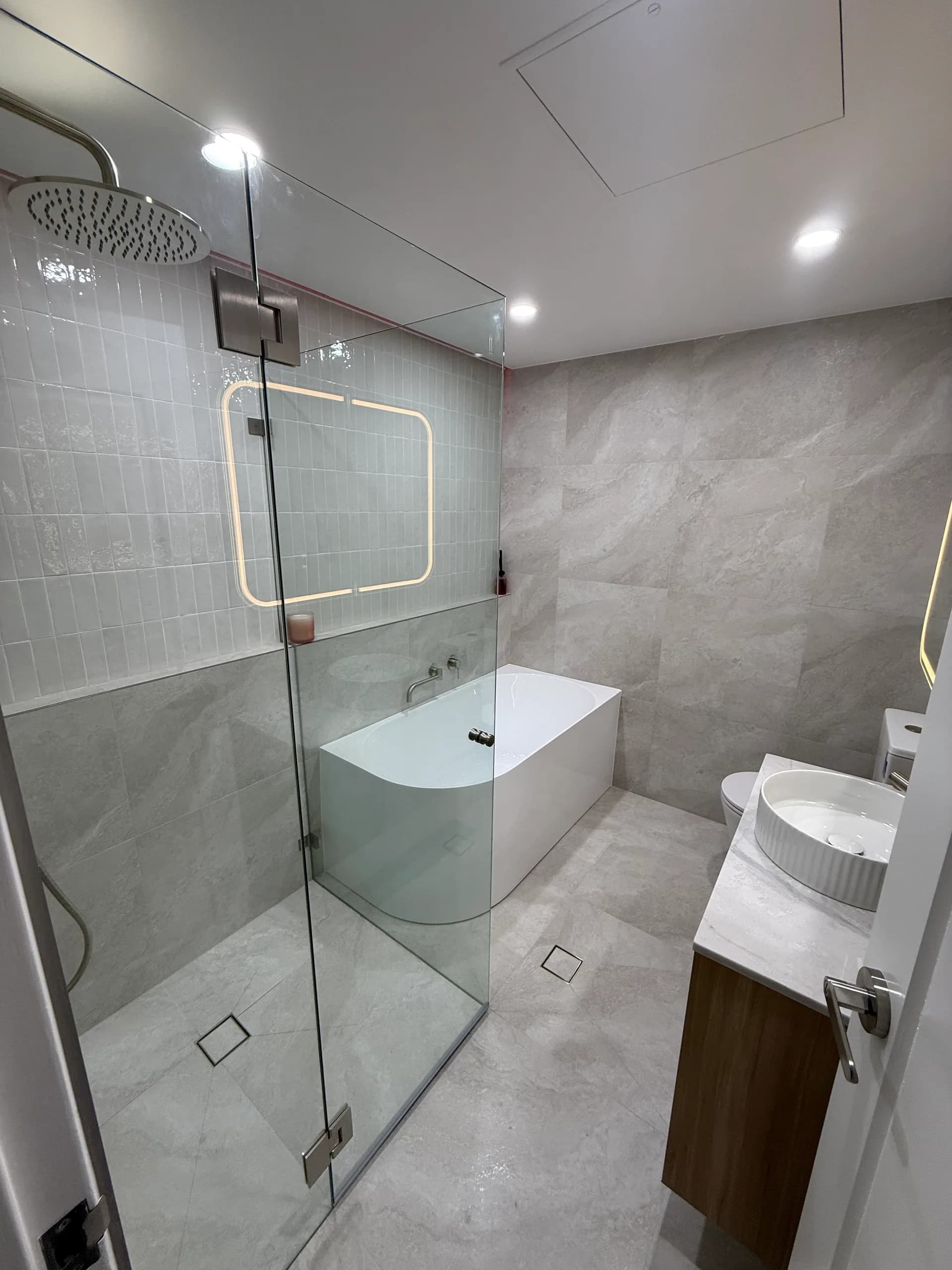 Renovated apartment bathroom with large-format tiling and a frameless glass shower screen