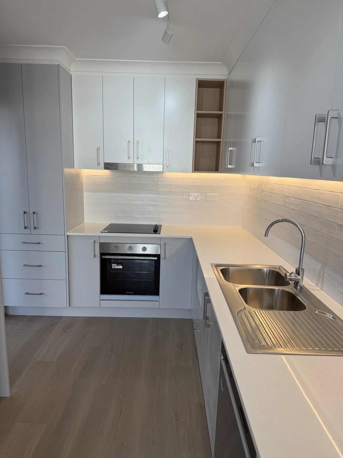 Ceramic cooktop and under-bench oven beside a double-bowl stainless steel sink
