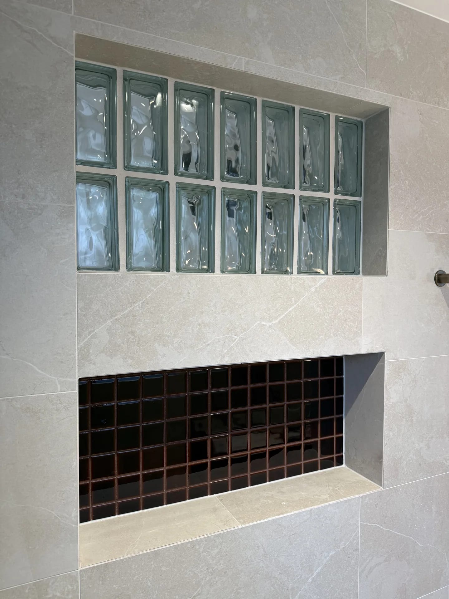Close view of a glass block panel above a recessed niche lined in dark brown gloss mosaic
