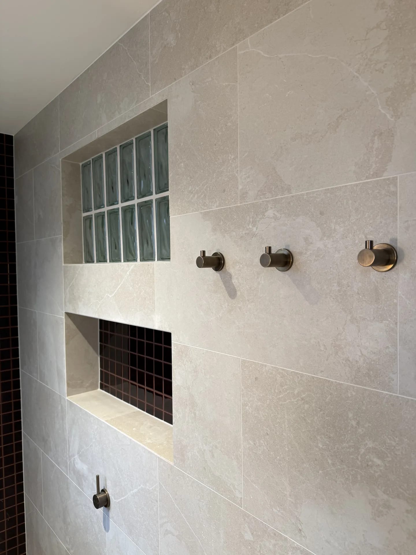 Stone-look tiled wall with a glass block panel, a dark mosaic niche and three bronze hooks