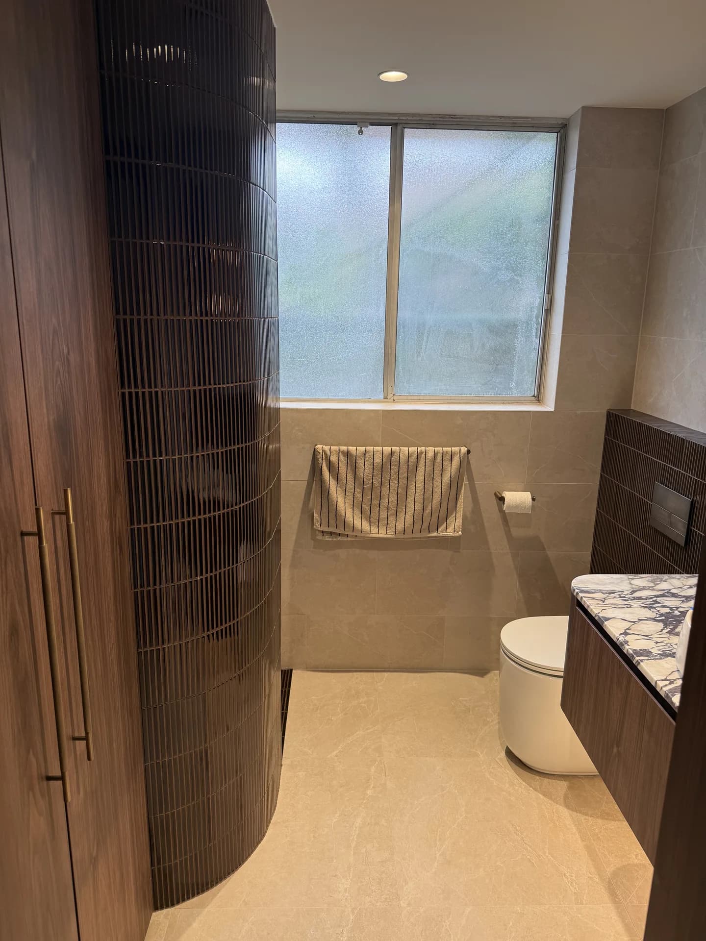 Renovated Bondi Beach bathroom with a curved dark tiled shower wall, walnut vanity and marble benchtop