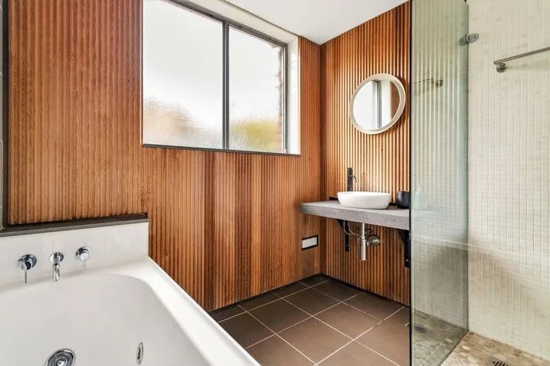 Original Bondi Beach bathroom with vertical timber batten walls, a spa bath under the window and brown floor tiles