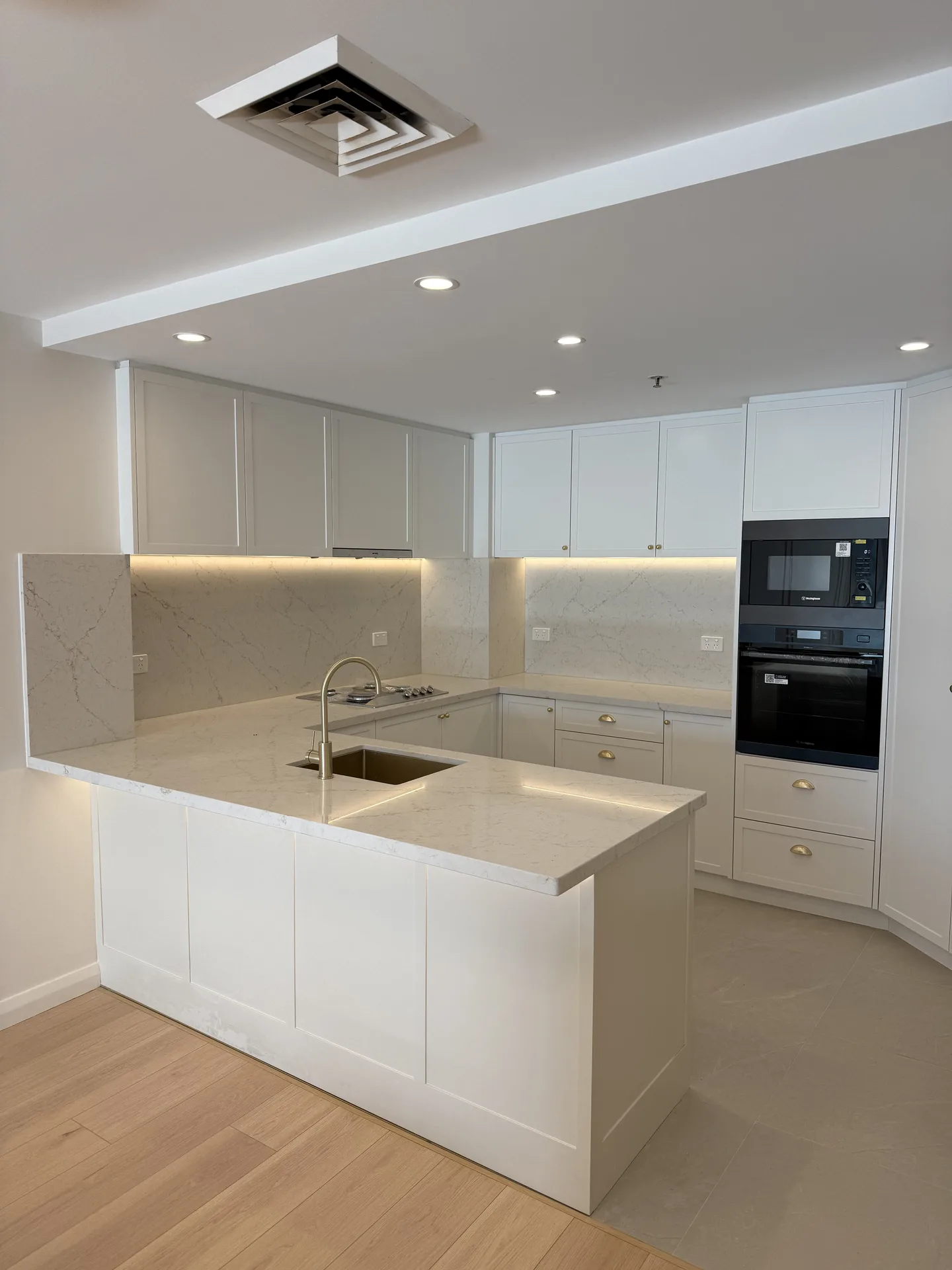 Kitchen peninsula with undermount sink, brass gooseneck tap and stacked black wall appliances