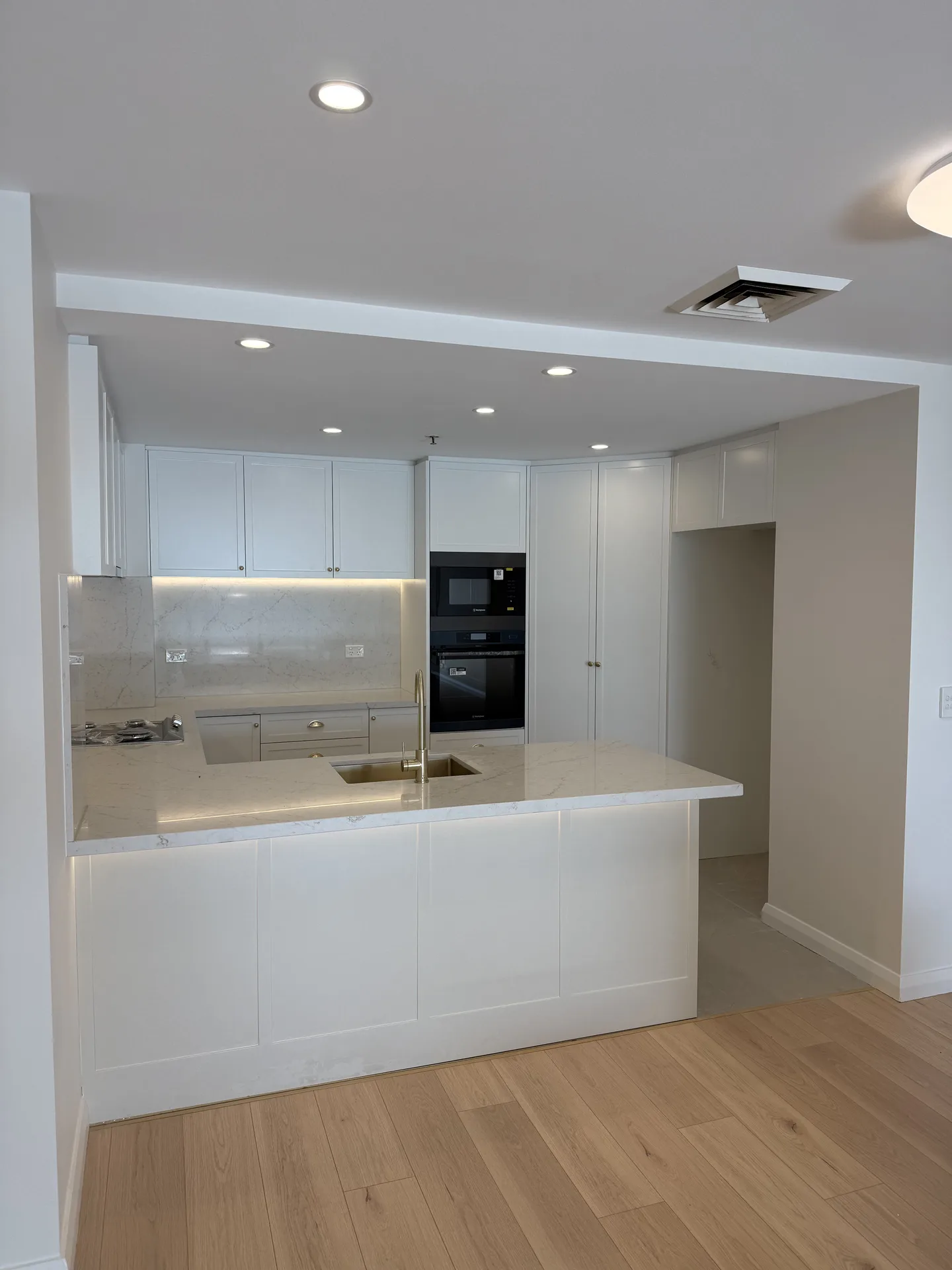 Kitchen seen from the living area with a floor-to-ceiling joinery run beside the appliance stack