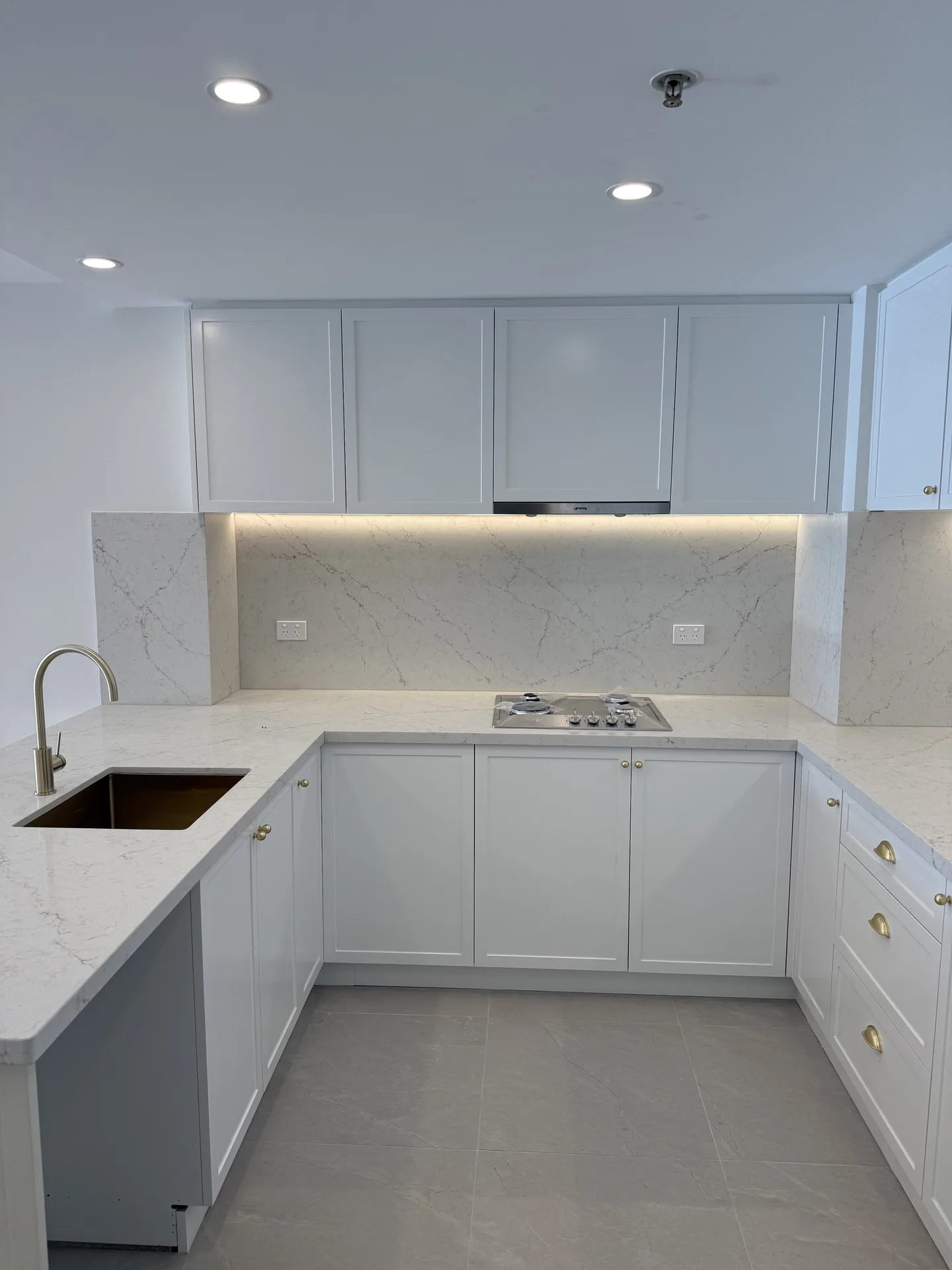 White shaker cabinetry with a full-height marble-look stone splashback and brushed brass handles