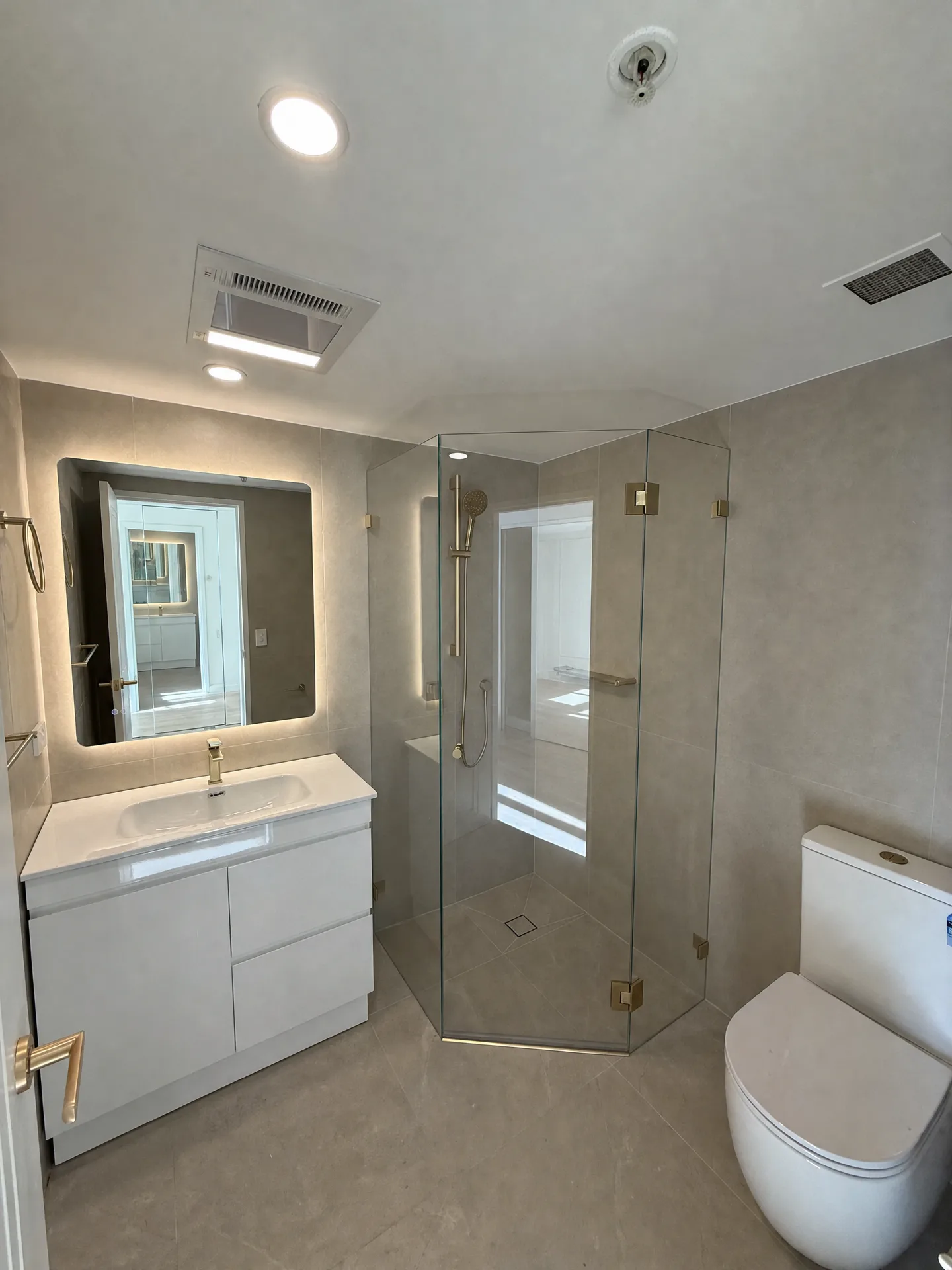 Wider view of the bathroom showing the angled shower, vanity and back-to-wall toilet