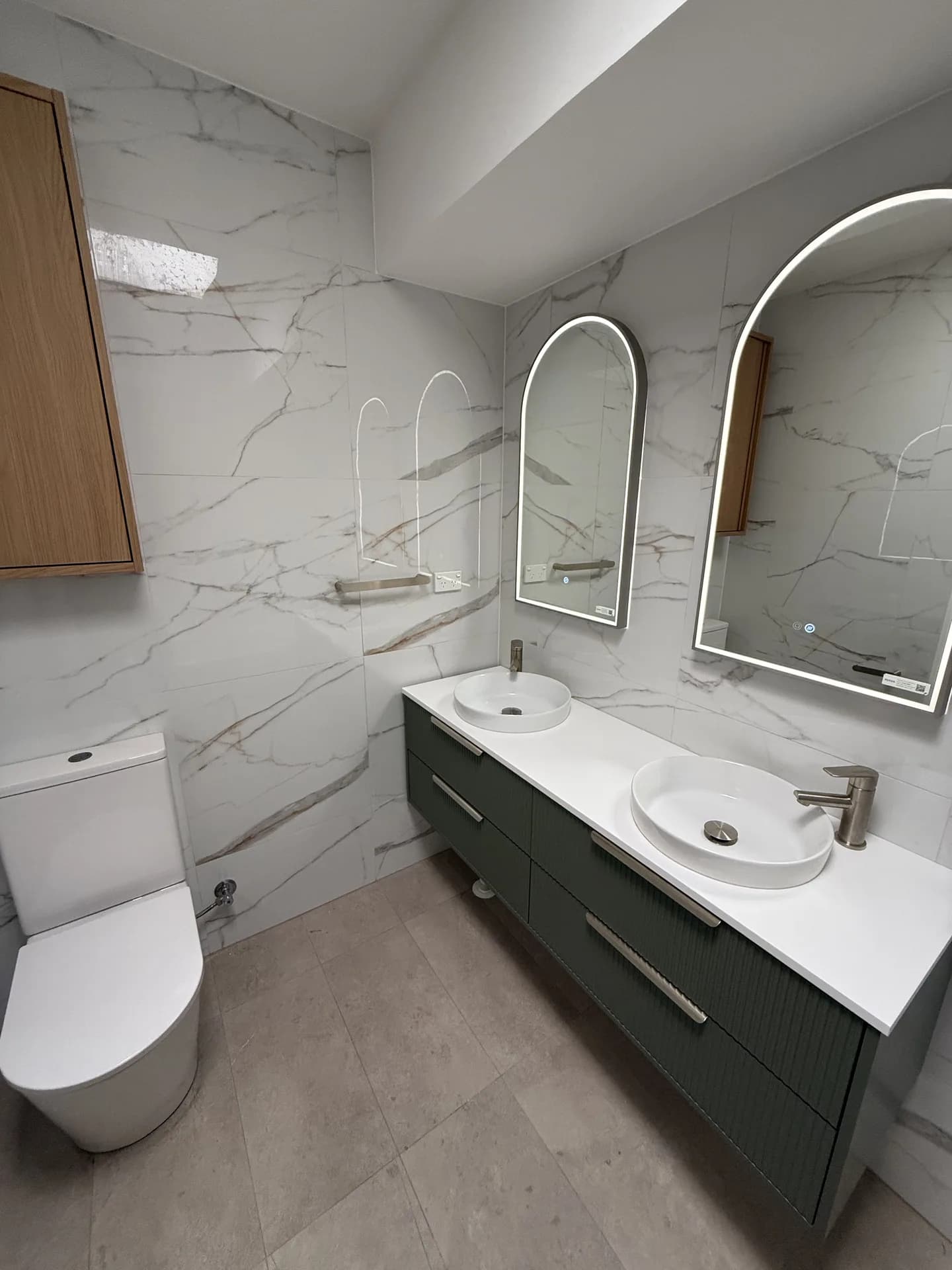 Apartment bathroom with marble-look walls, an olive fluted double vanity and two arched LED mirrors