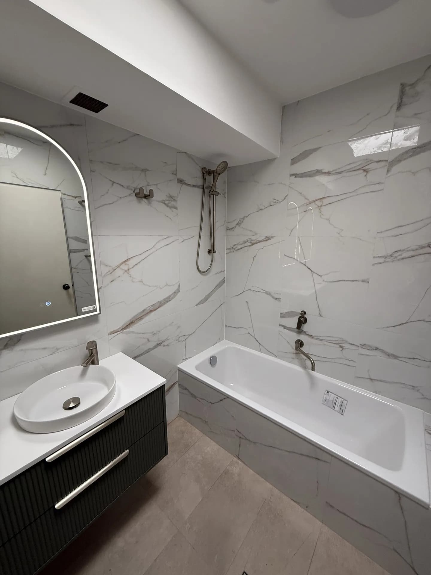Inset bath against marble-look tiling with a handheld shower on a rail above it