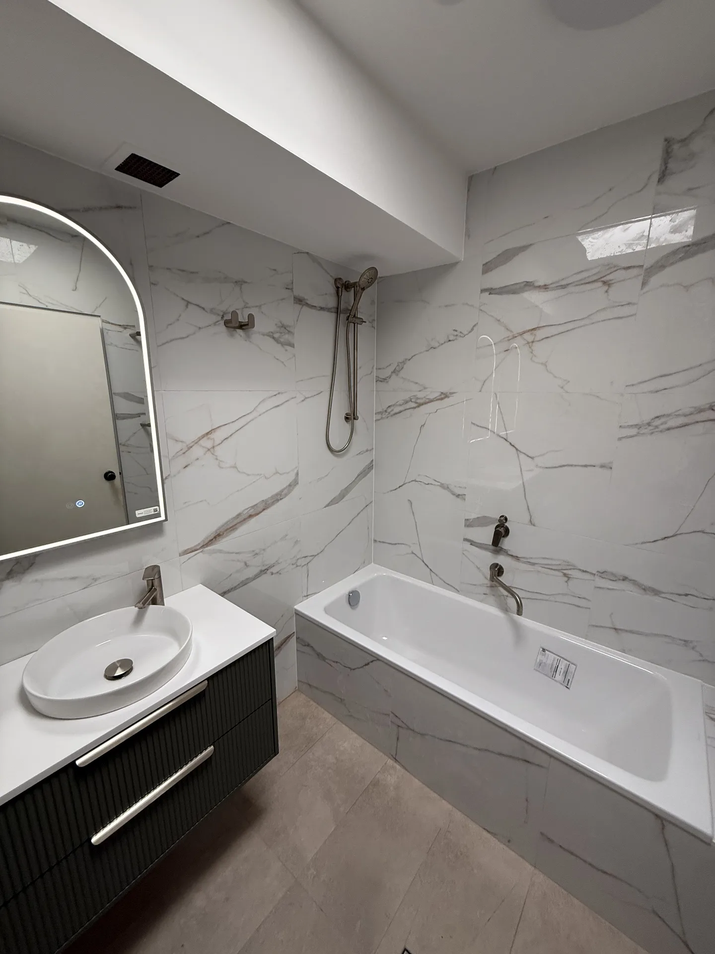 Inset bath against marble-look tiling with a handheld shower on a rail above it