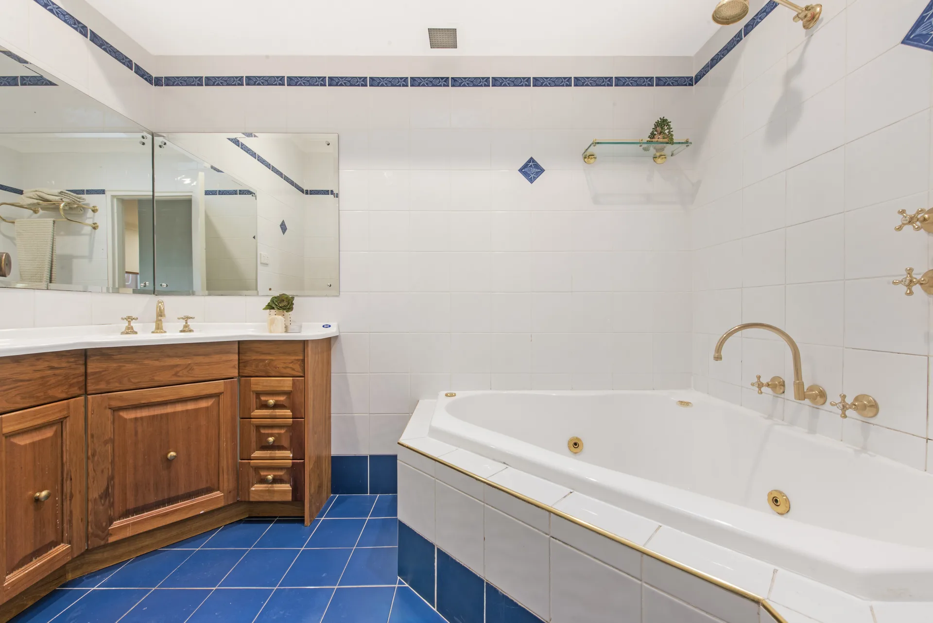 Original bathroom with blue floor tiles, timber vanity, brass taps and a corner spa bath