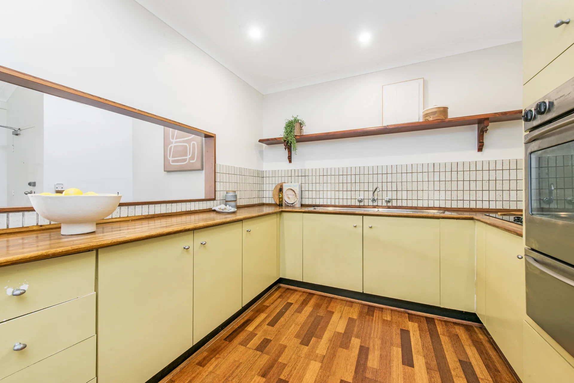 Original kitchen with cream laminate doors, timber benchtop and small square tiled splashback