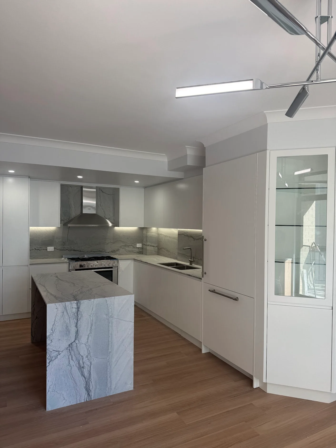 Waterfall island beside a white kitchen and tall glass-front display cabinet in Kogarah