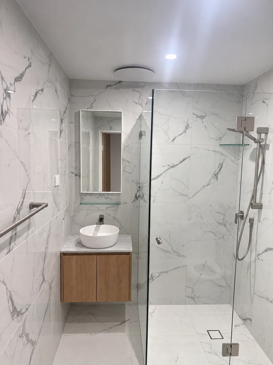 Kogarah bathroom with marble-look wall tiles, clear shower screen and floating timber vanity