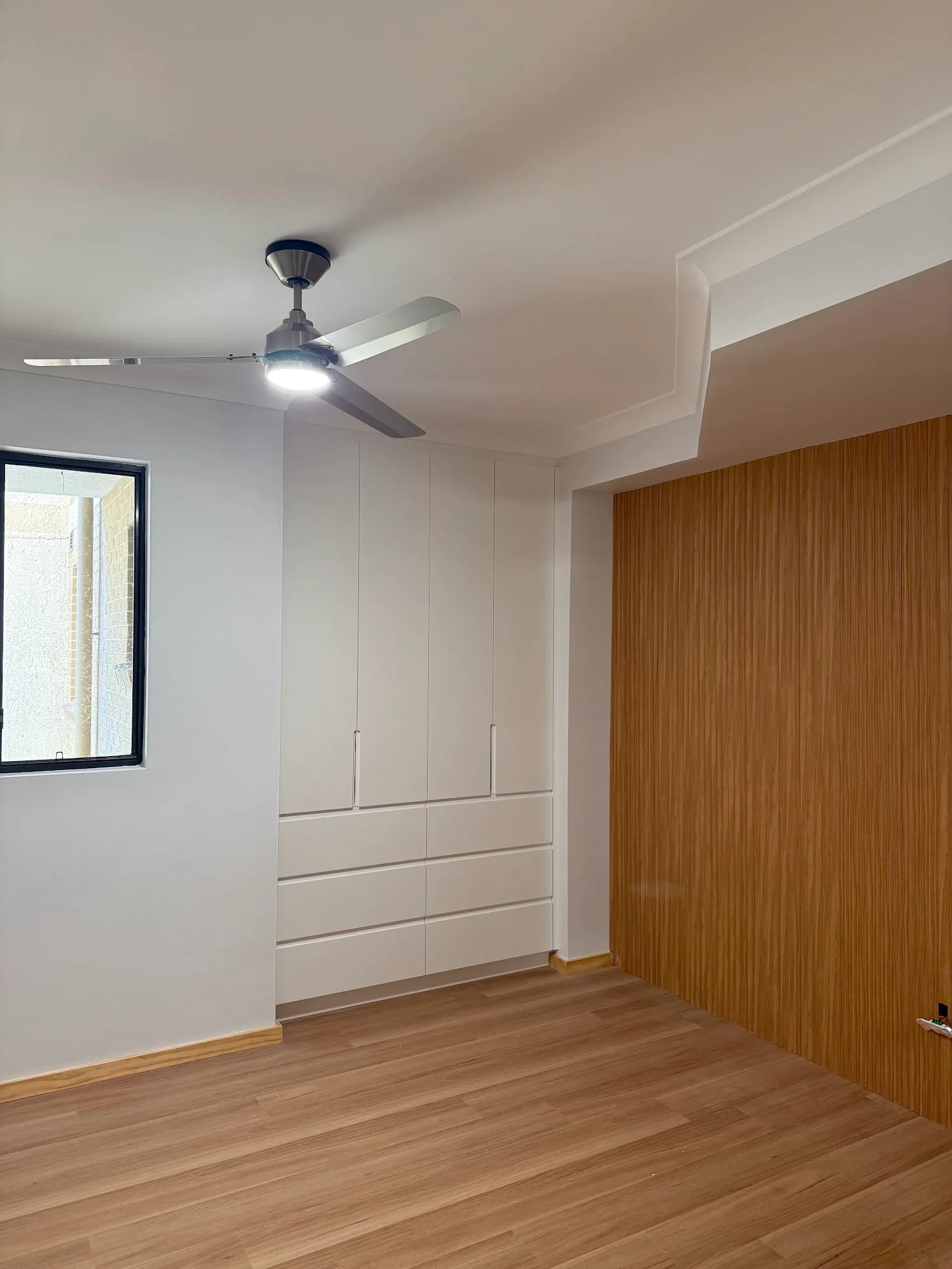 White built-in bedroom wardrobe with drawers, pale timber-look floor and vertical timber feature panel