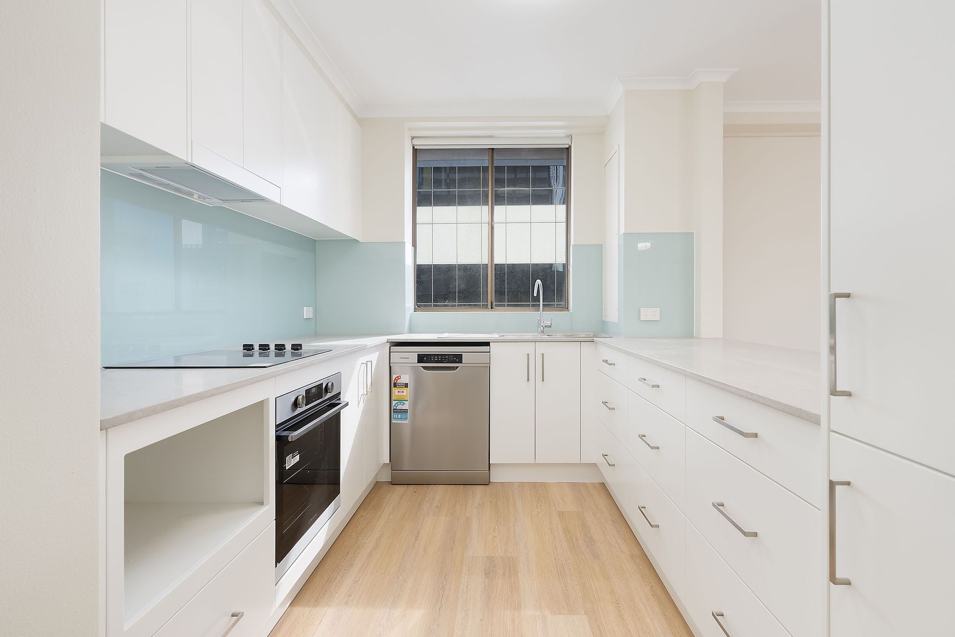 Renovated kitchen in a Sydney high-rise apartment, with white cabinetry and a glass splashback