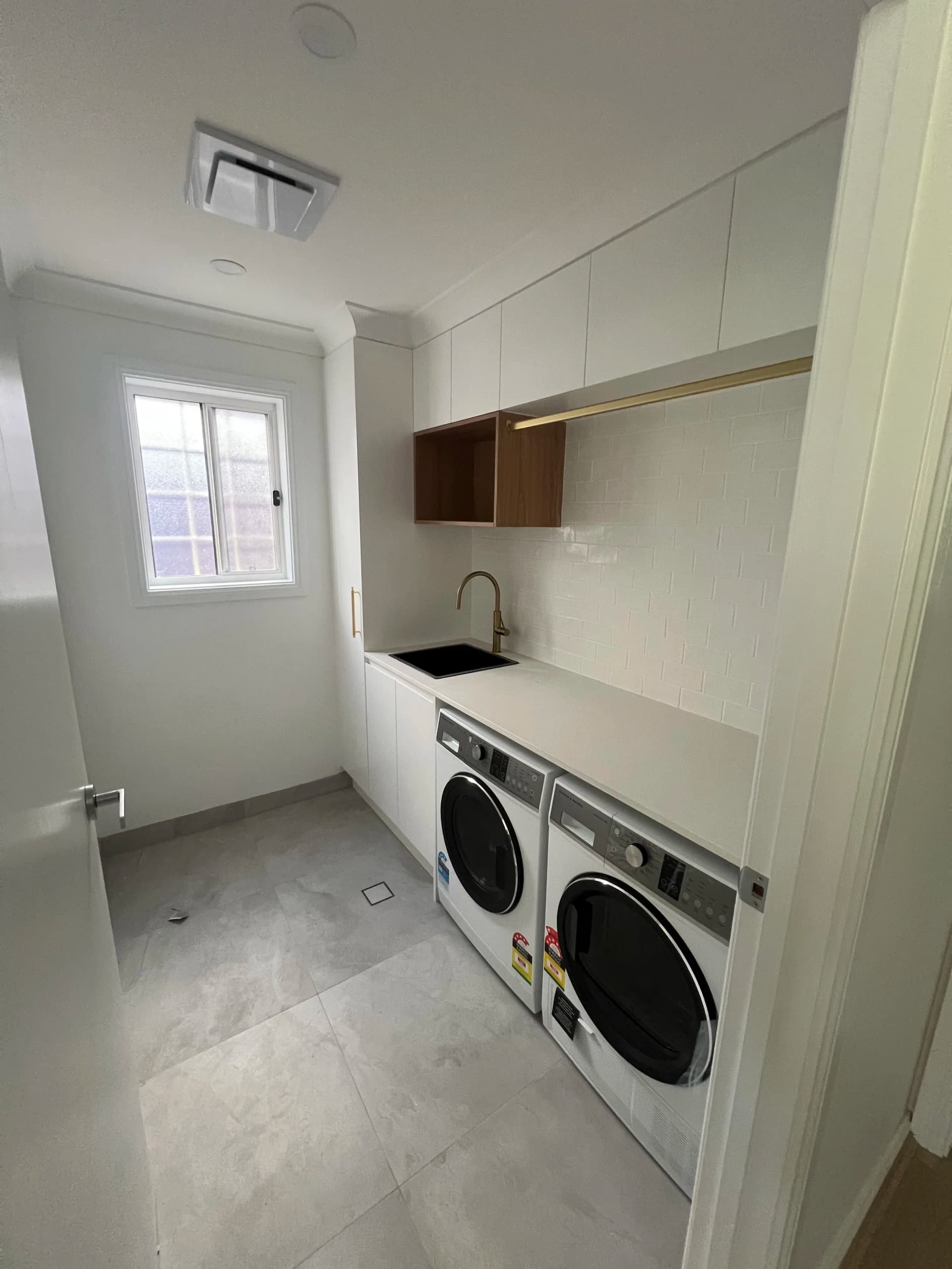 Renovated North Strathfield laundry with white cabinetry, a black sink and timber shelving