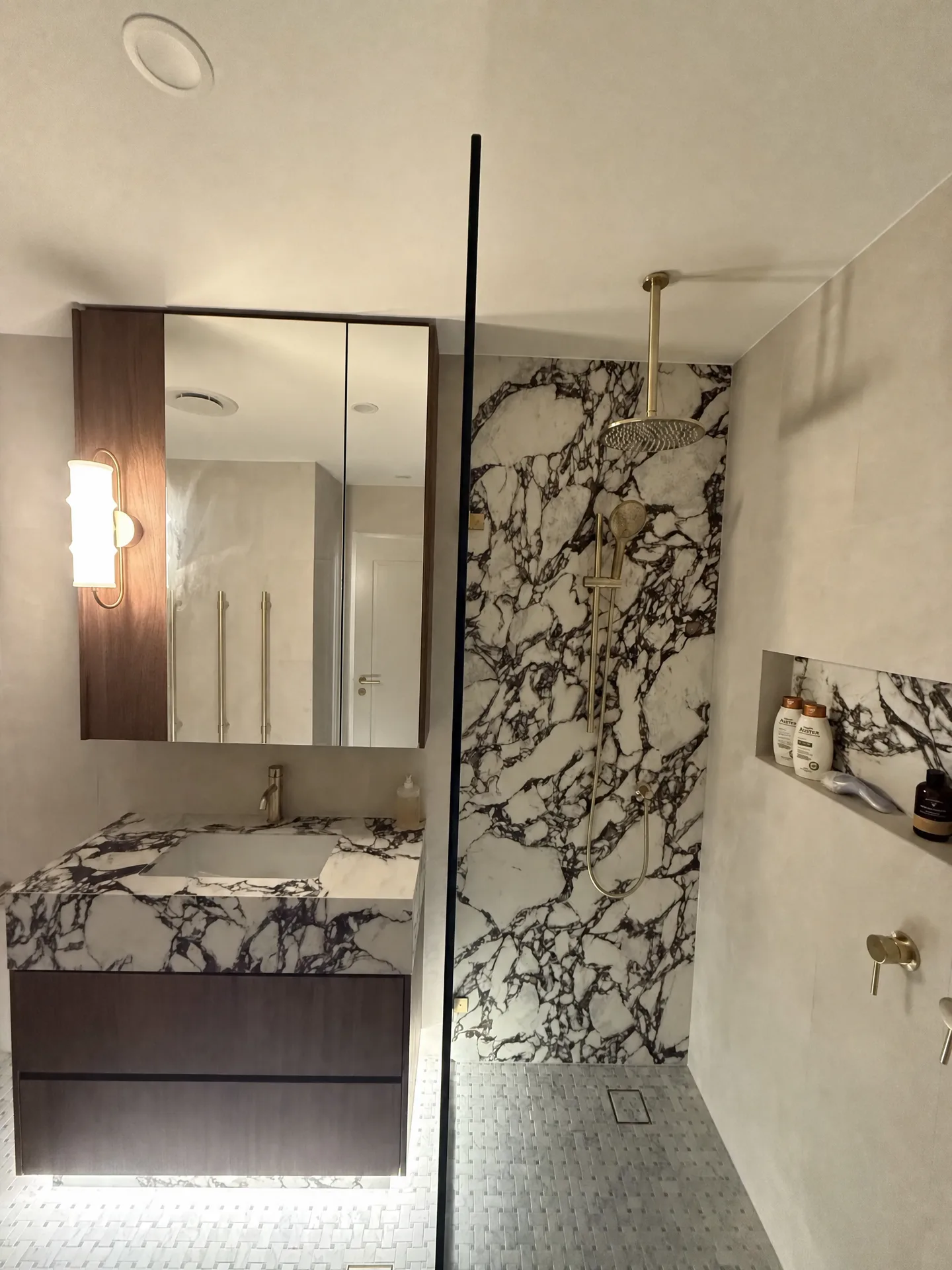 Full-height purple-veined marble shower wall beside a floating marble-topped vanity