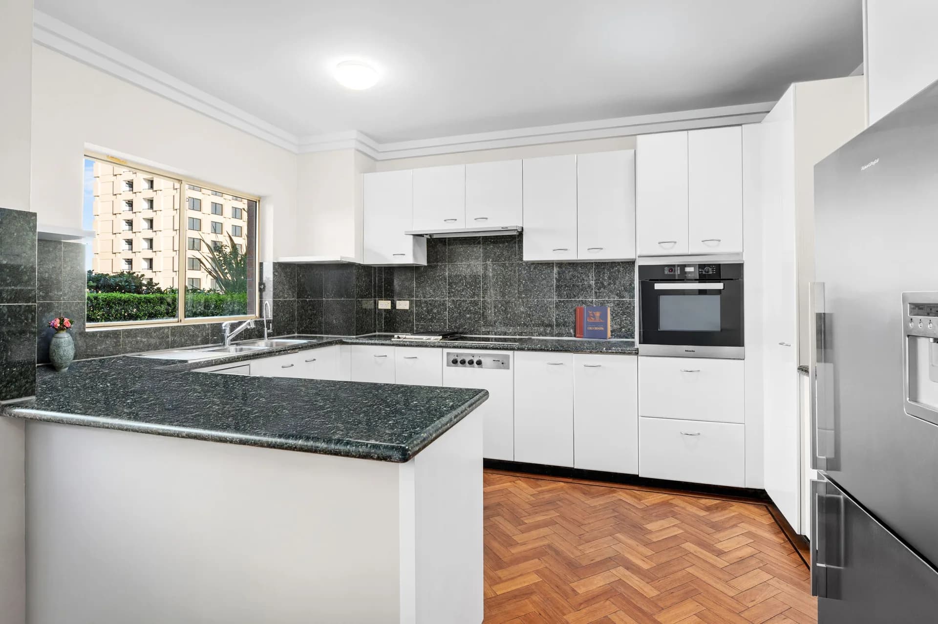 Original North Sydney apartment kitchen with white laminate doors, dark green granite benchtops and a parquet floor