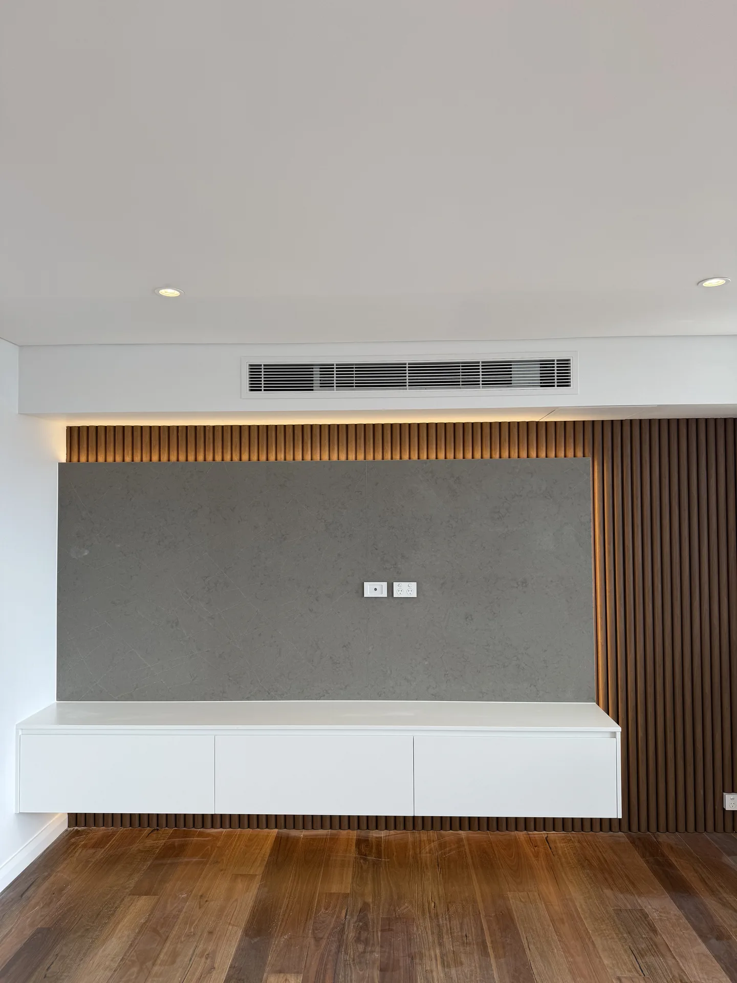 Living room media wall with a stone-look panel, vertical timber battens and a floating white console