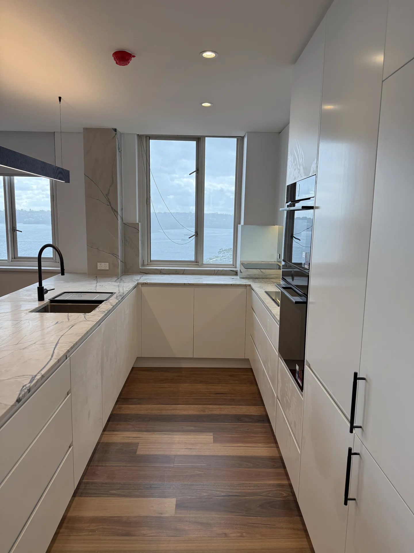 Kitchen bench run in white joinery and stone turning the corner under a harbour-facing window
