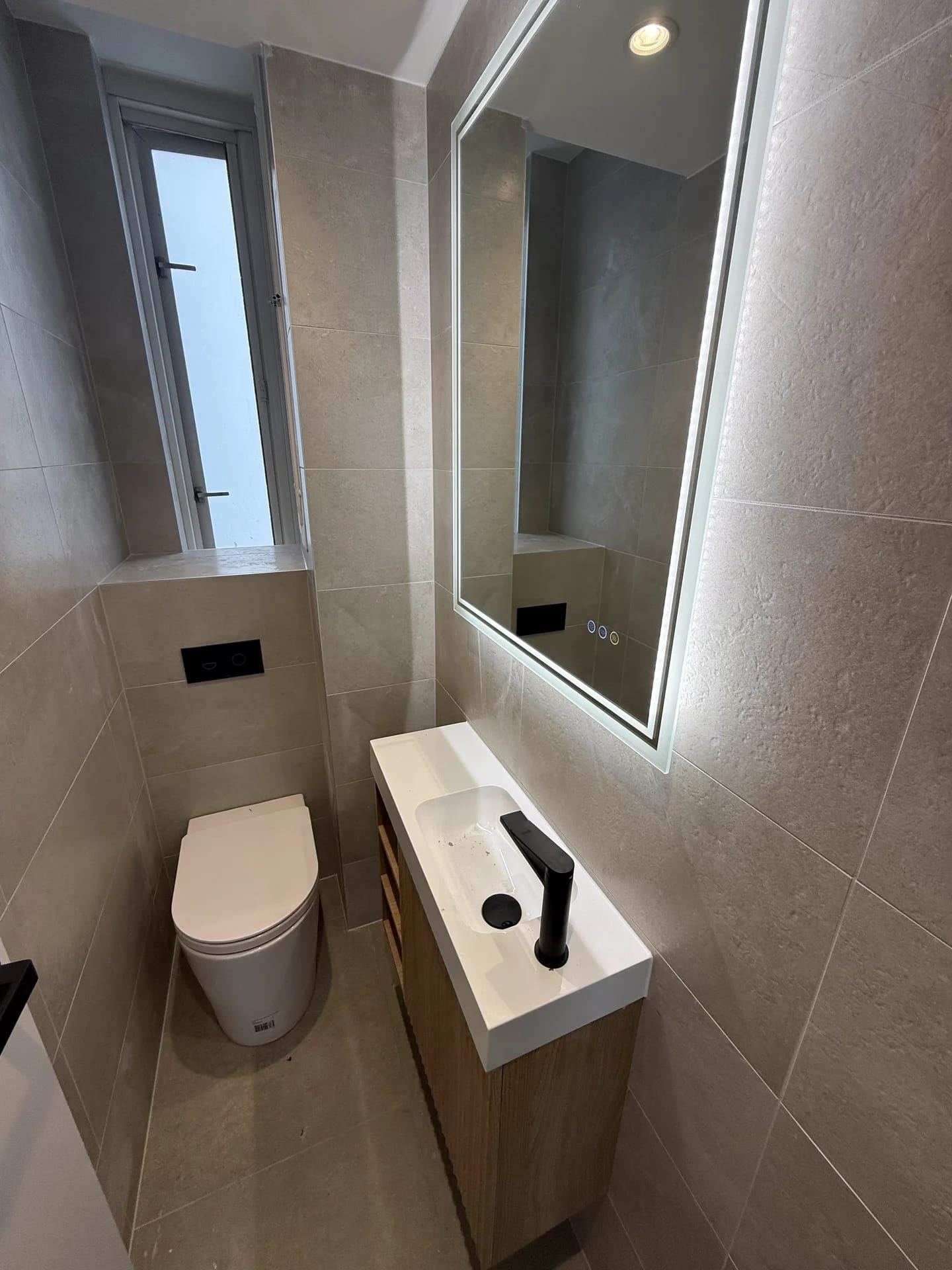 Powder room with a slim timber vanity, backlit LED mirror, wall-hung pan and stone-look tiles