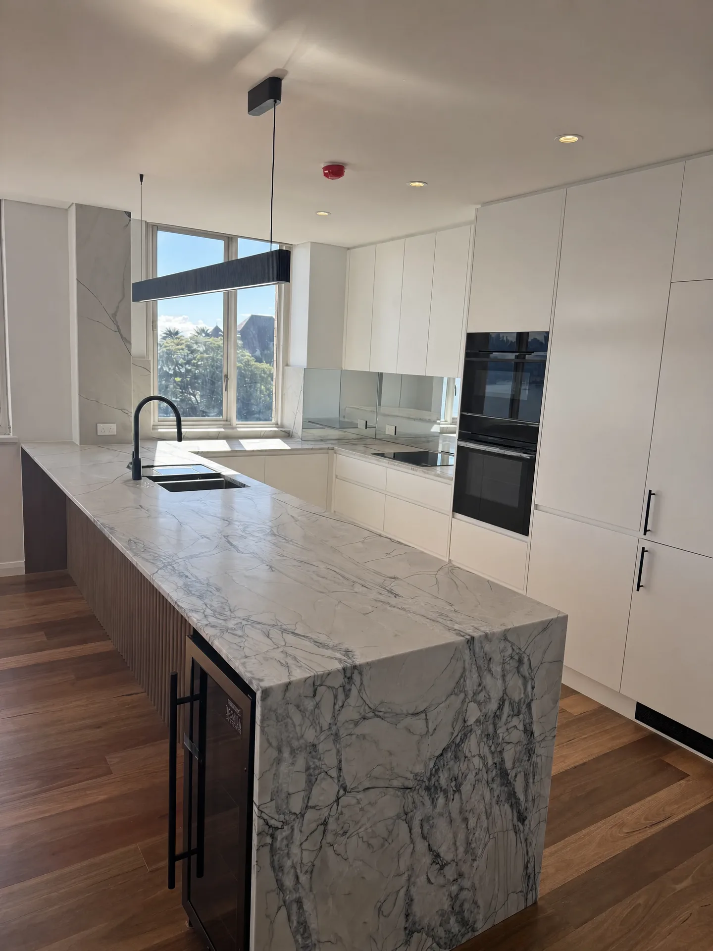 Renovated Point Piper apartment kitchen with a marble-look stone island and full-height white joinery