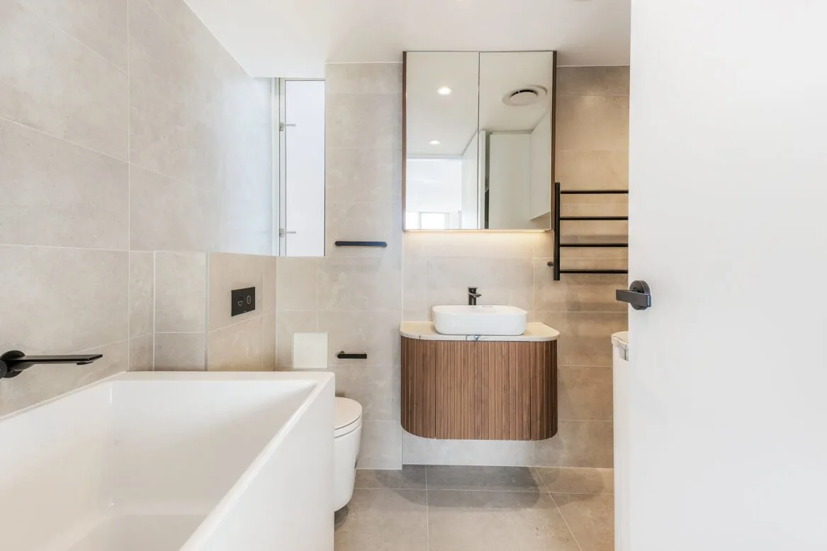 Main bathroom with a built-in bath, curved timber vanity, above-counter basin and black tapware