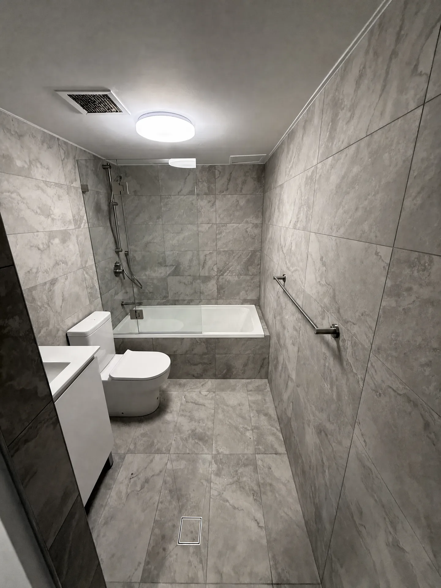 Bathroom tiled floor to ceiling in grey marble-look porcelain with inset bath