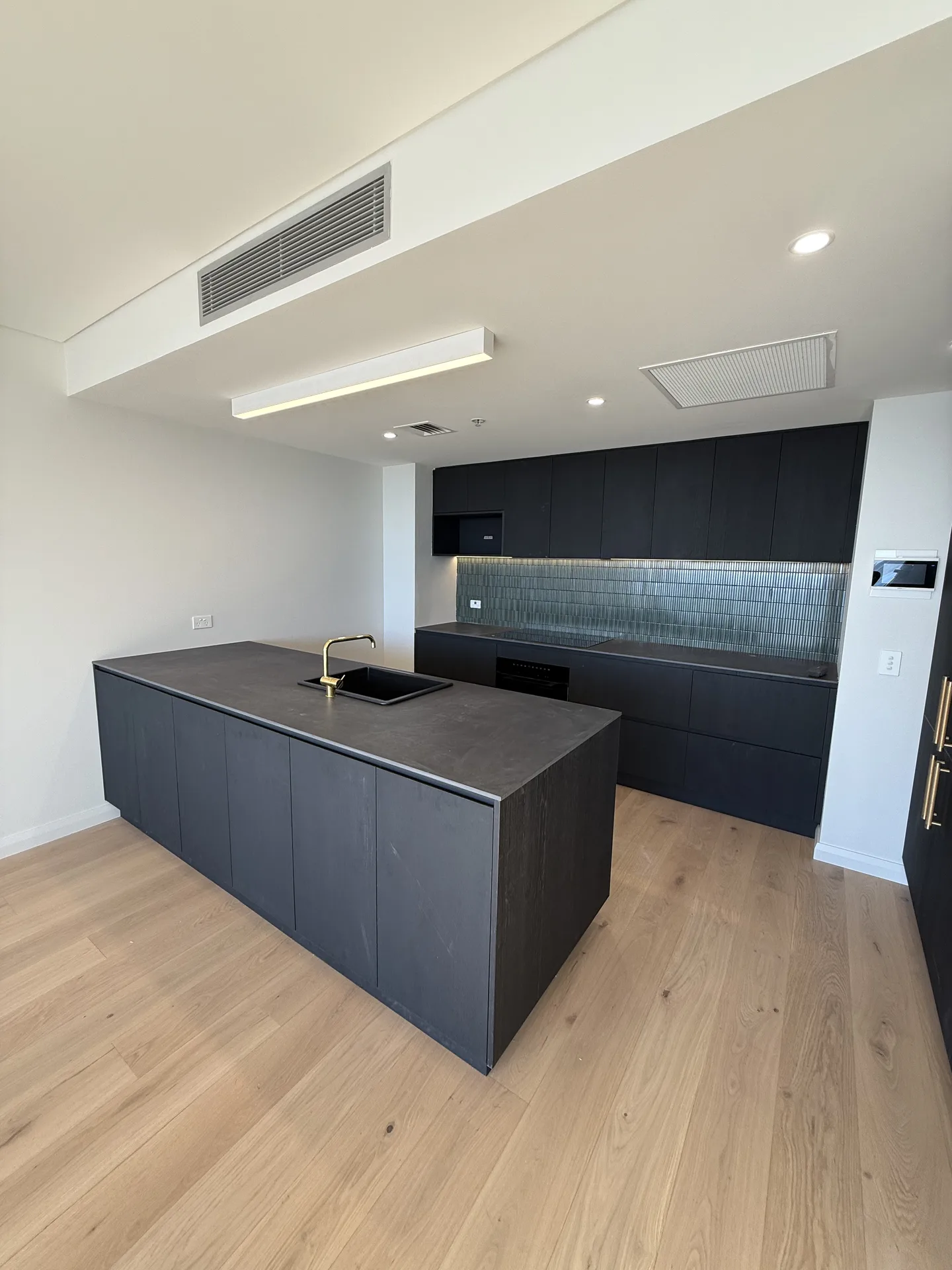 Charcoal kitchen island with a dark stone-look benchtop and brass mixer tap