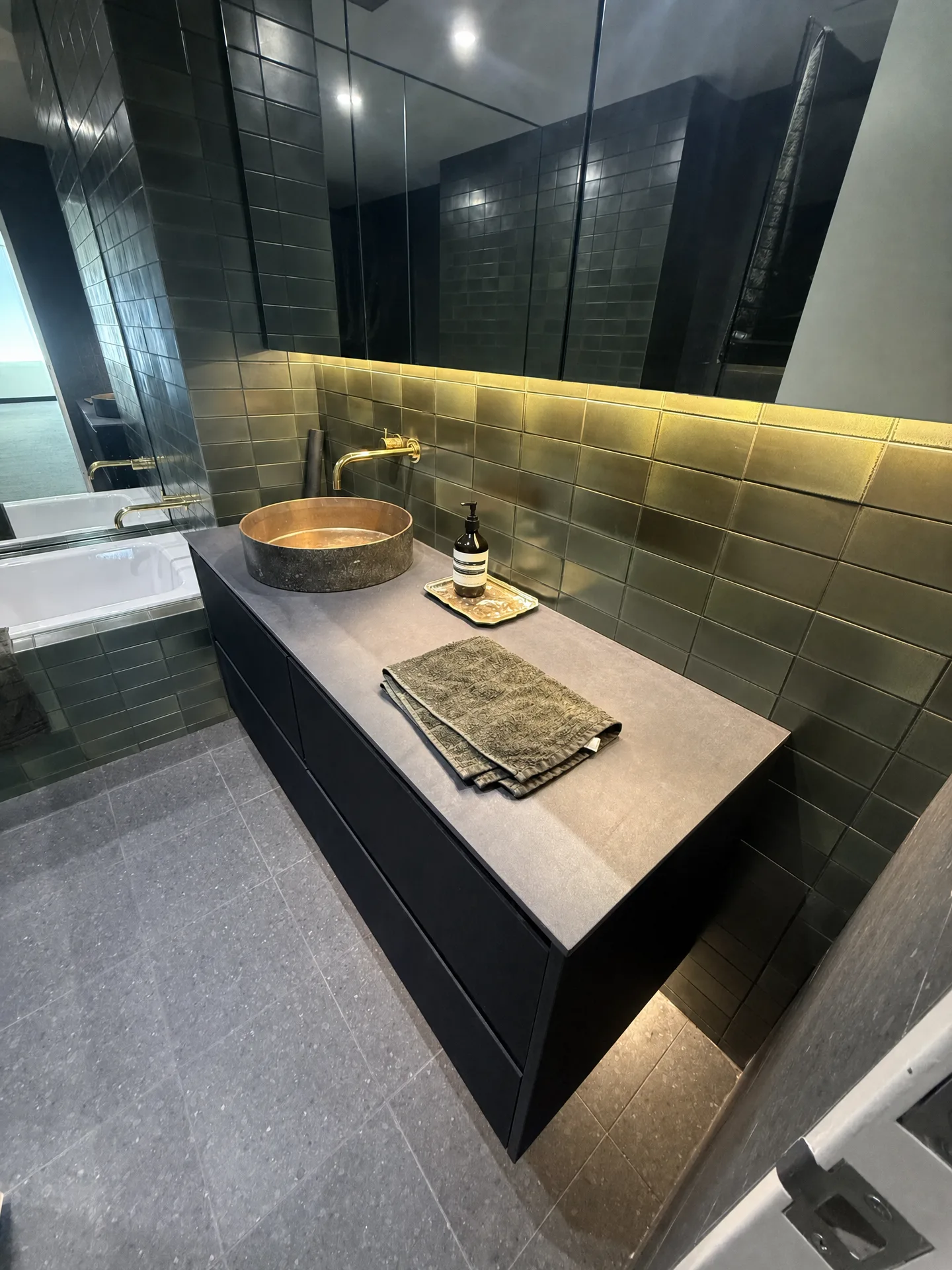 Black floating vanity with a round copper basin and brass wall-mounted tapware