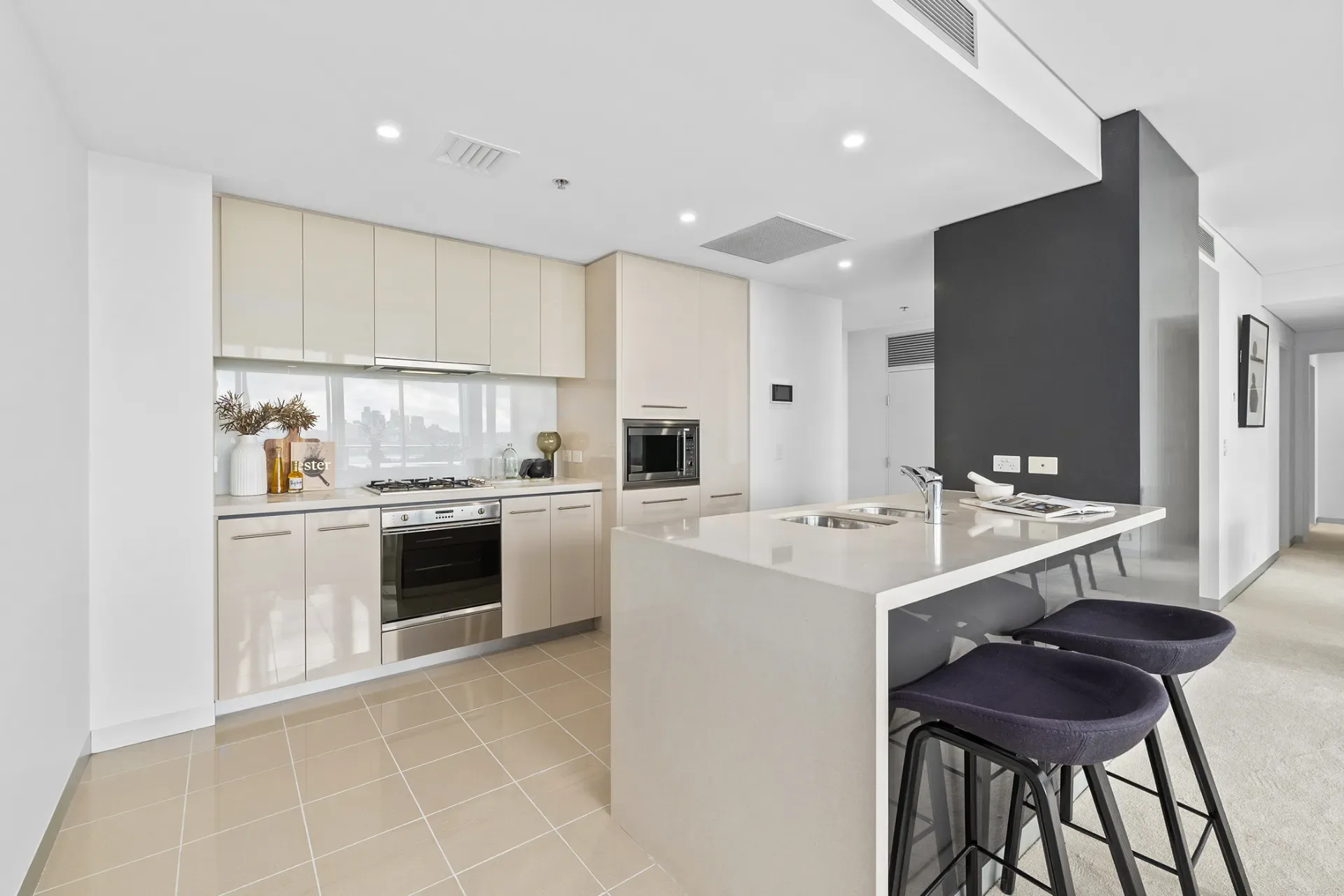 Original cream gloss kitchen with a stone peninsula, bar stools and beige floor tiles