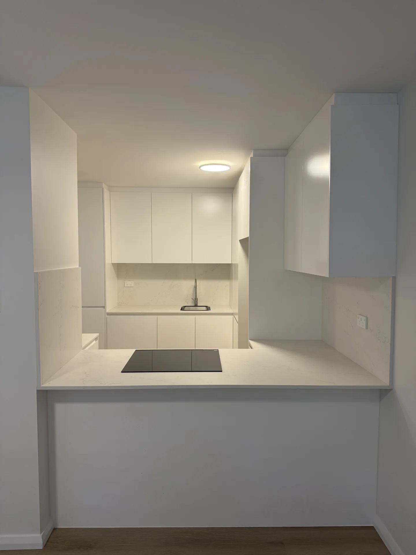 Compact all-white Randwick apartment kitchen with an induction cooktop on a stone peninsula
