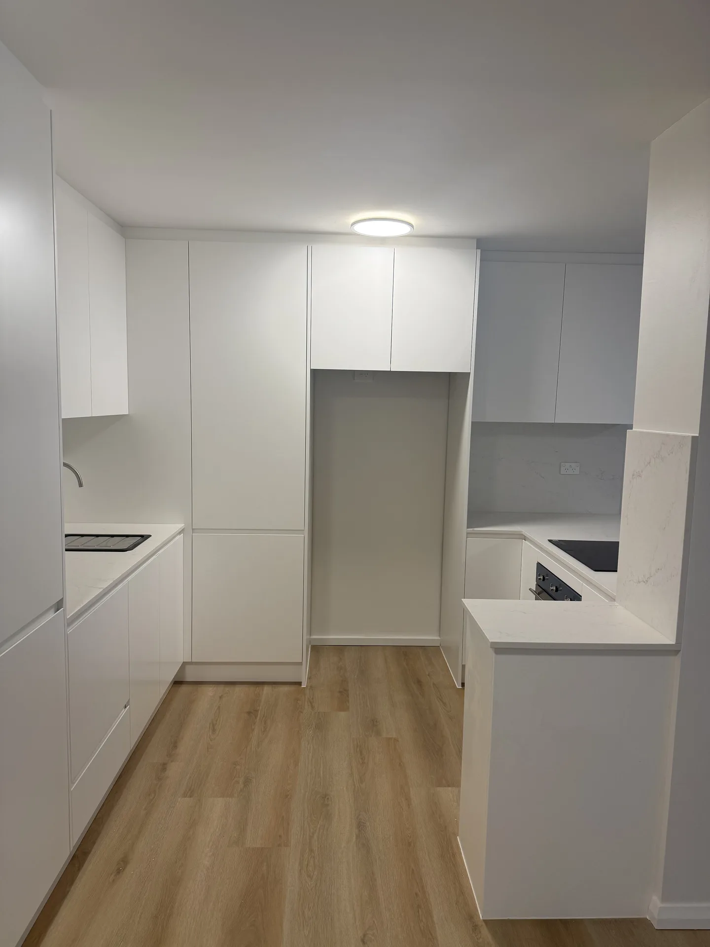 Minimalist white handleless Randwick apartment kitchen with timber-look flooring