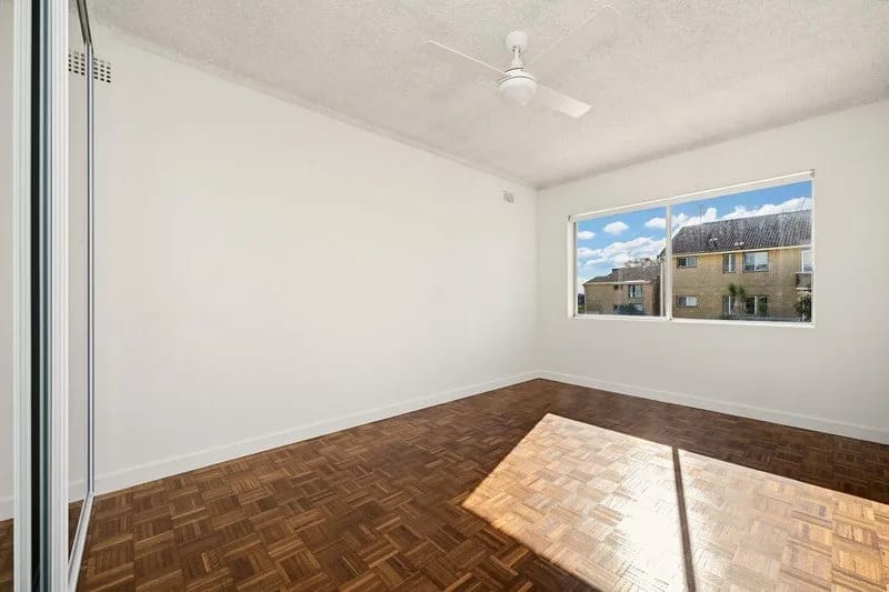 Bedroom with original parquet floor, ceiling fan and window over neighbouring rooftops