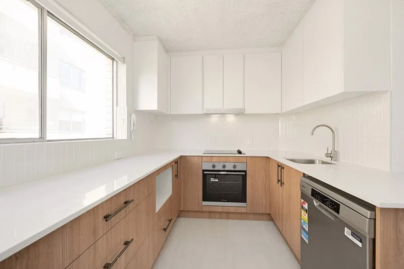 Renovated U-shaped kitchen in a Randwick walk-up apartment, with timber-look base cabinets and a white benchtop