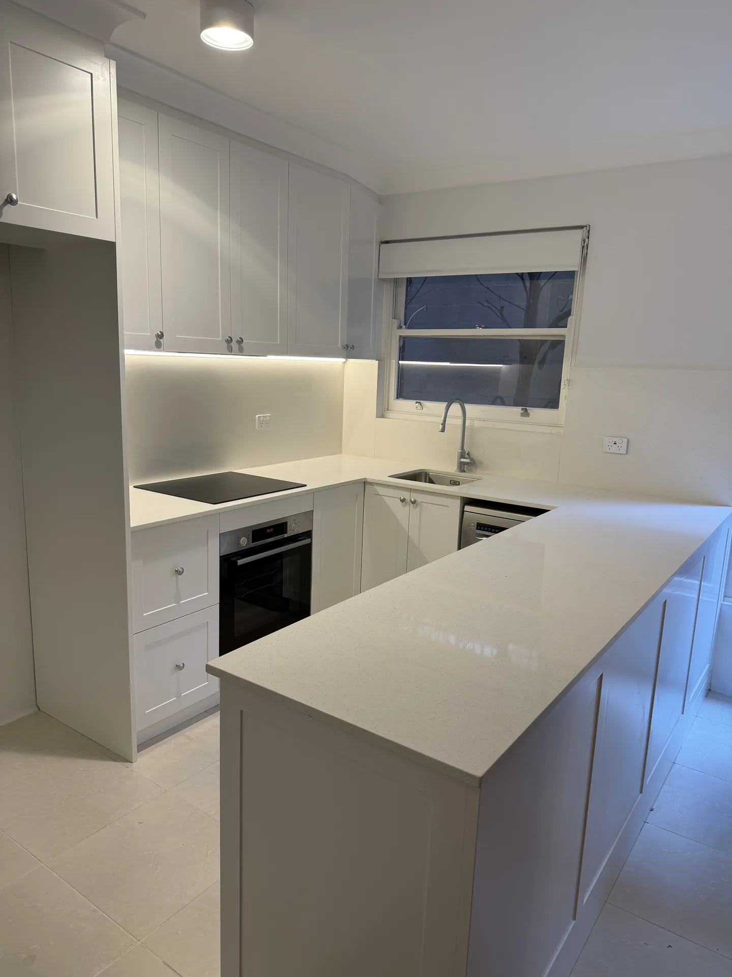 Renovated white shaker kitchen with a stone-look peninsula bench in a Ryde apartment