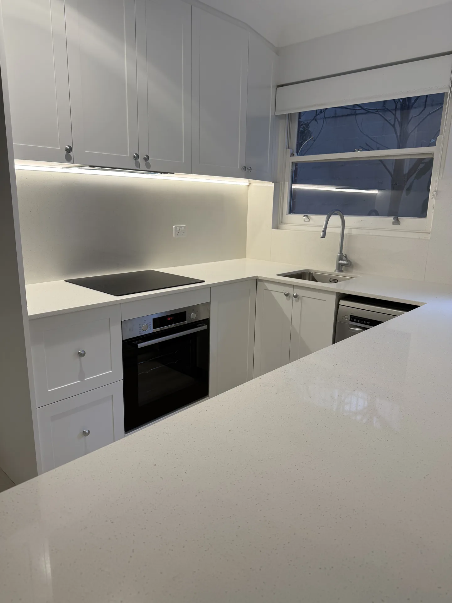 White shaker overhead cupboards with an LED strip lighting a stone-look splashback