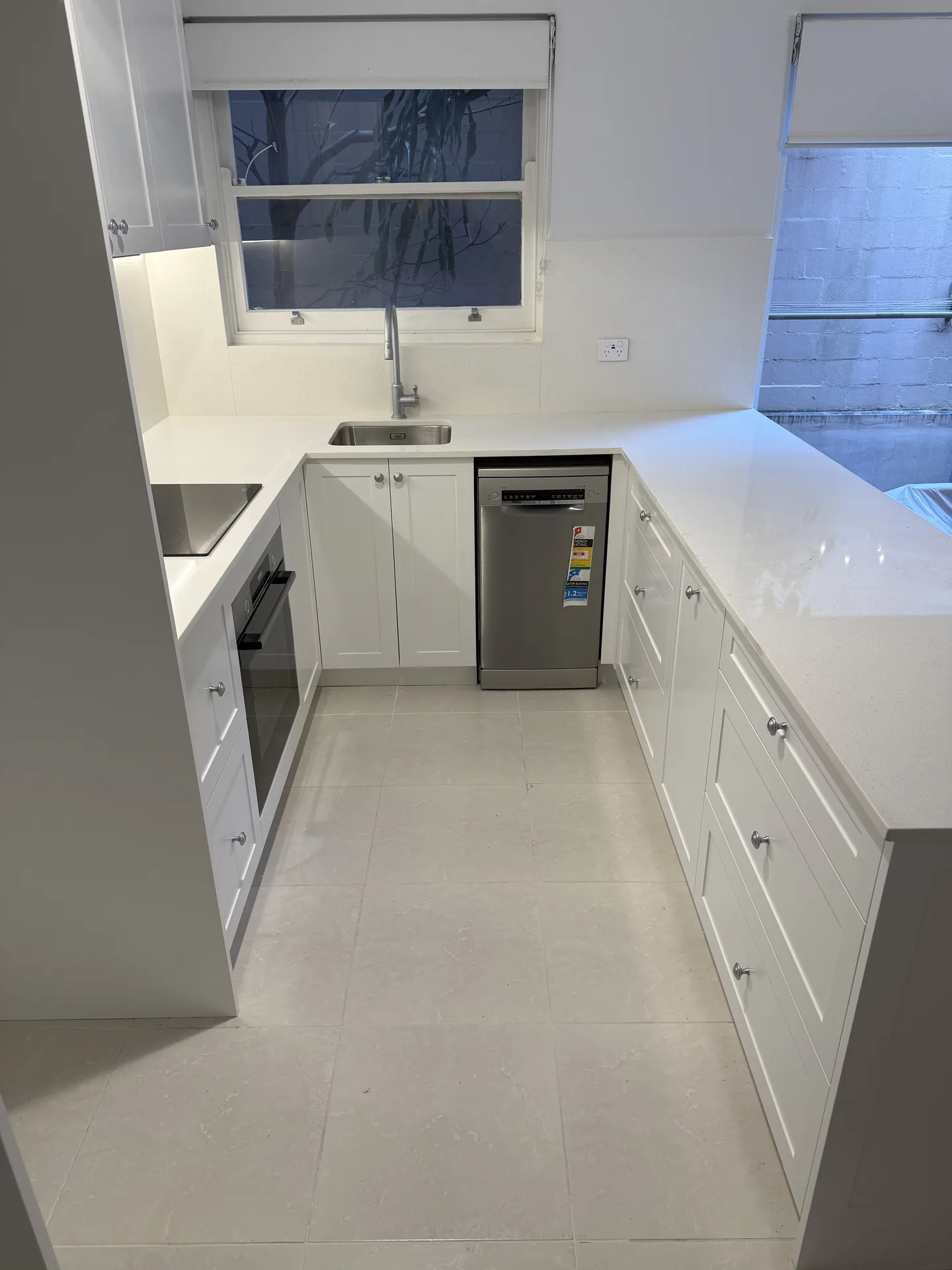 Compact U-shaped white kitchen with a slimline dishwasher and stone-look floor tiles