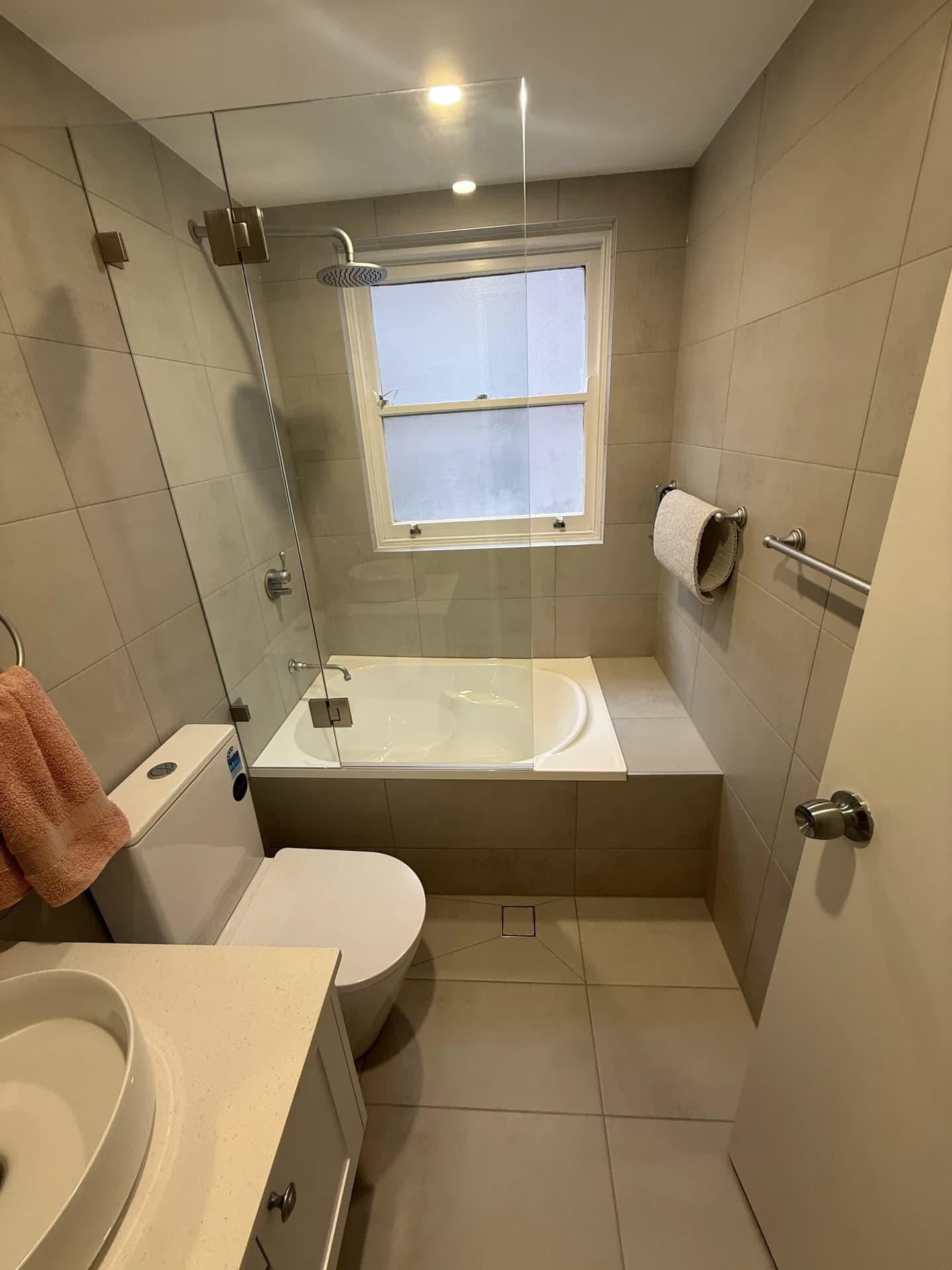 Inset bath under a window with a frameless glass screen and a rain head above it