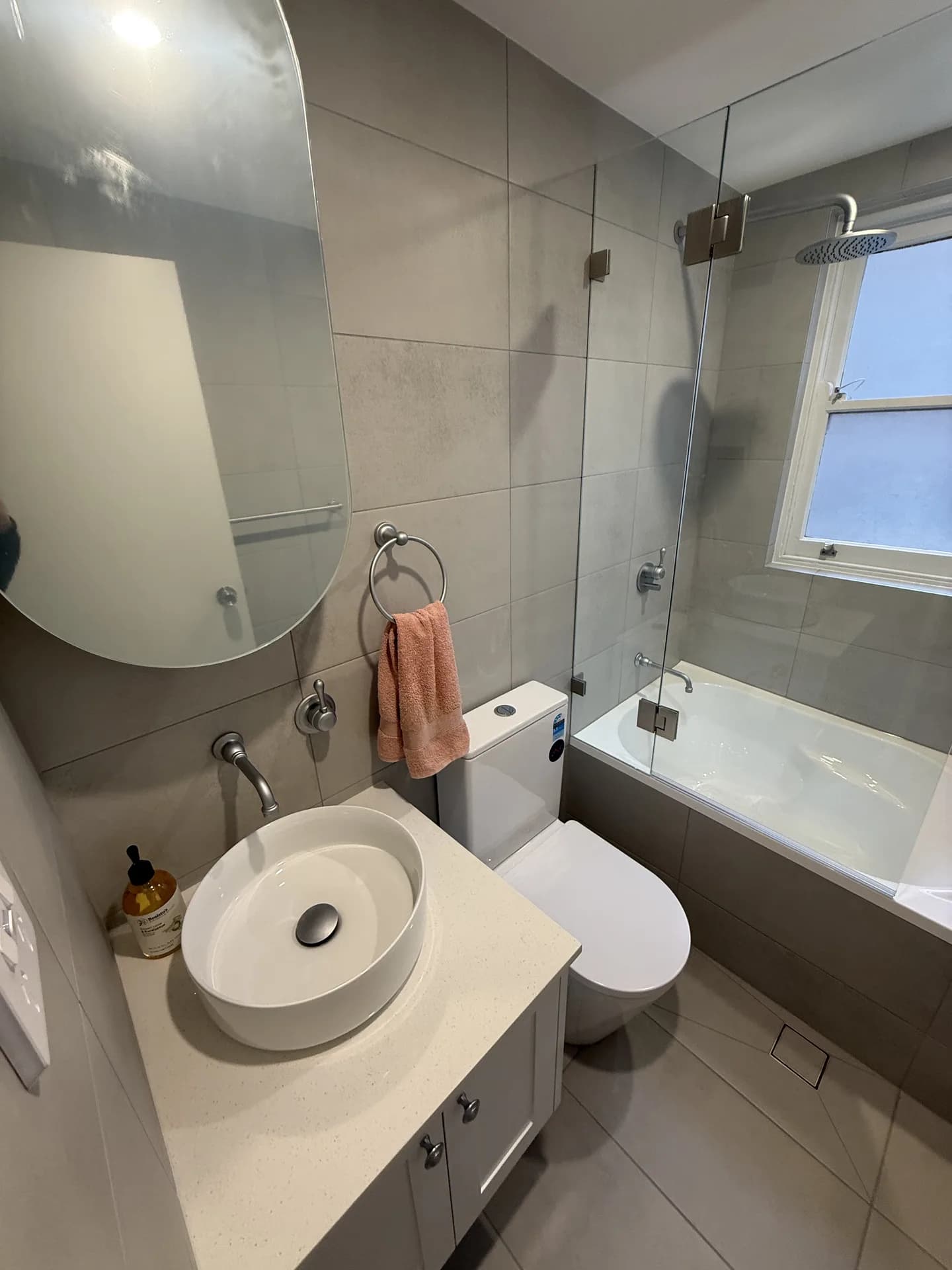 Compact Ryde apartment bathroom with a round vessel basin, oval mirror and a bath with a glass screen