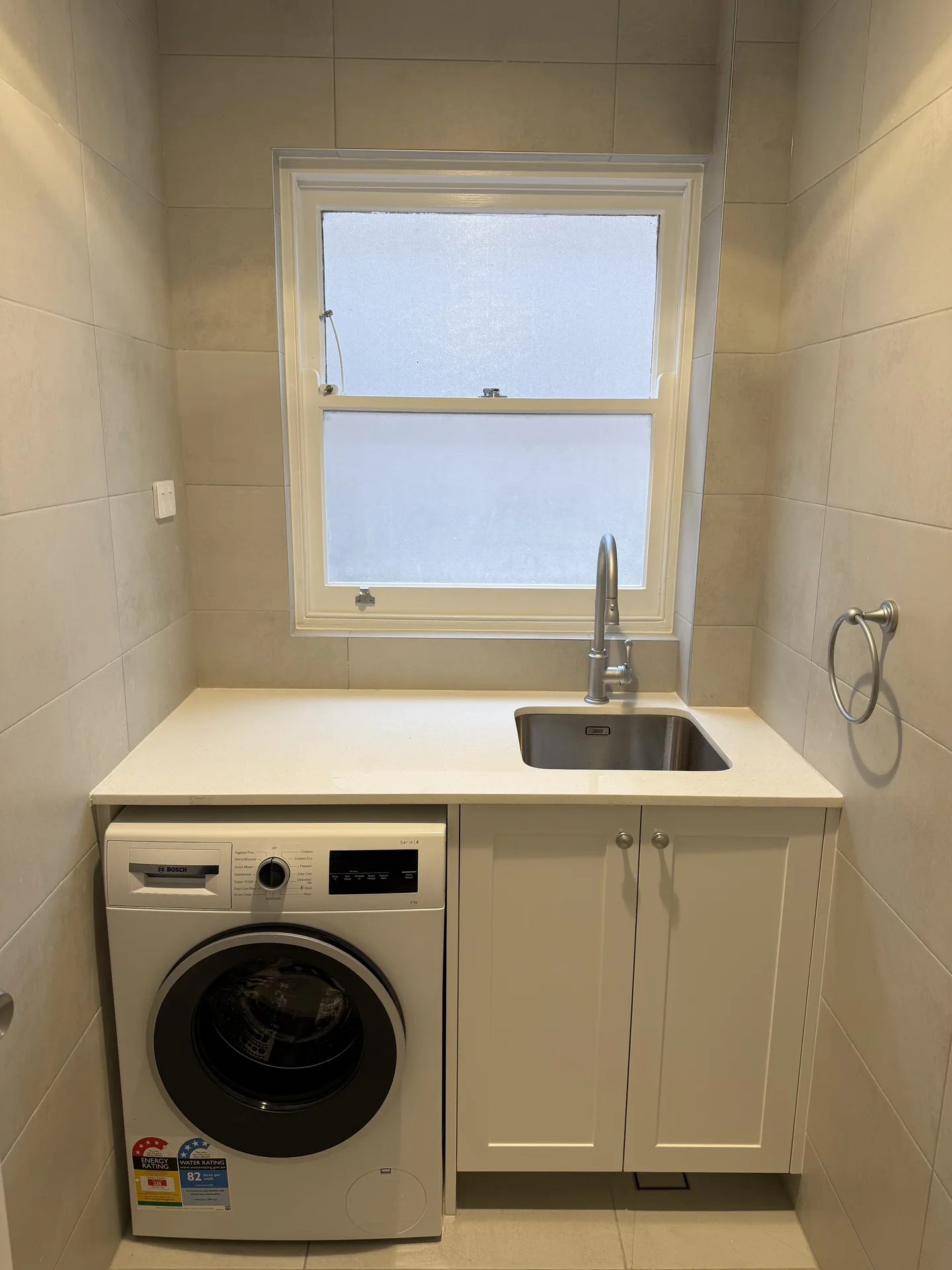 Laundry nook with a stone-look bench over a front-loader and a sink under the window
