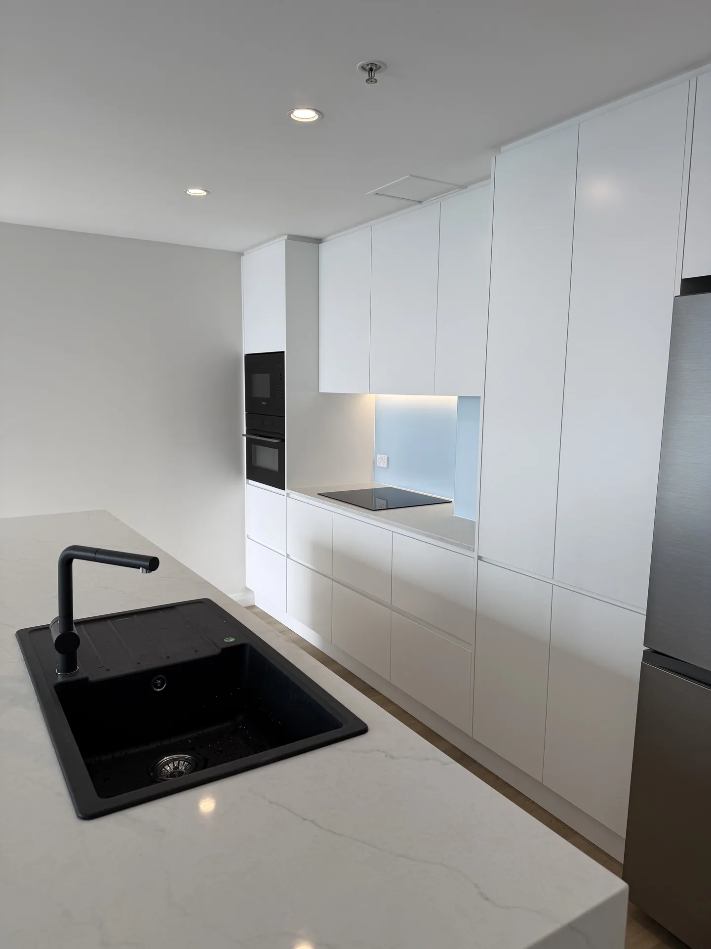 Black composite sink and pull-out mixer in stone benchtop with white joinery wall beyond