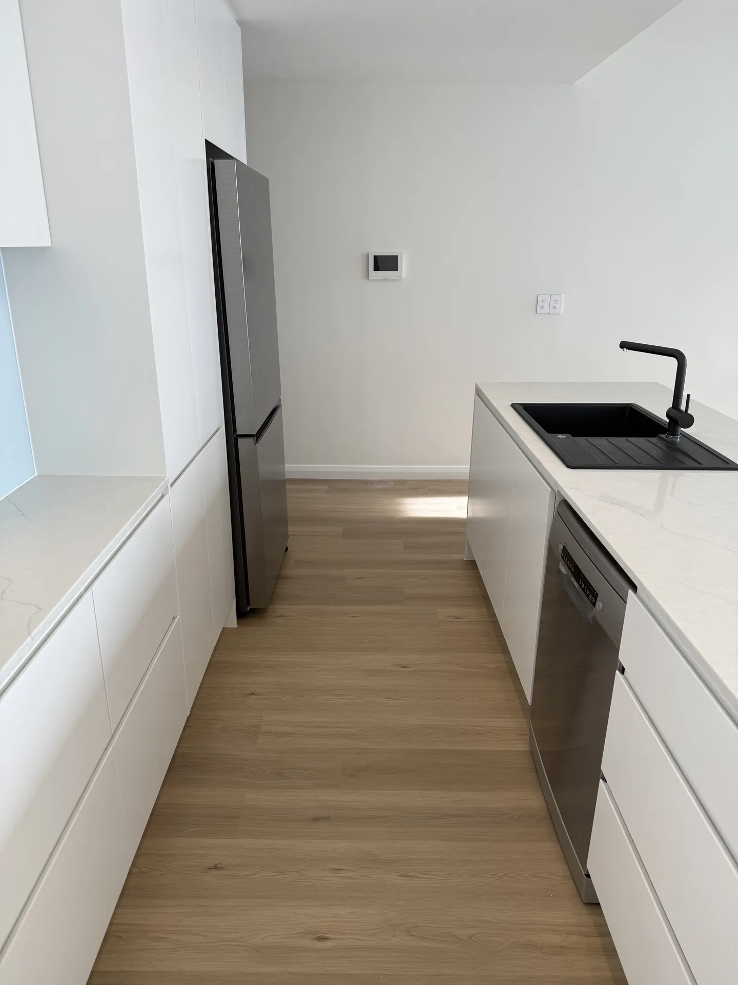 Island run with black sink and stainless dishwasher opposite tall white cabinetry and fridge