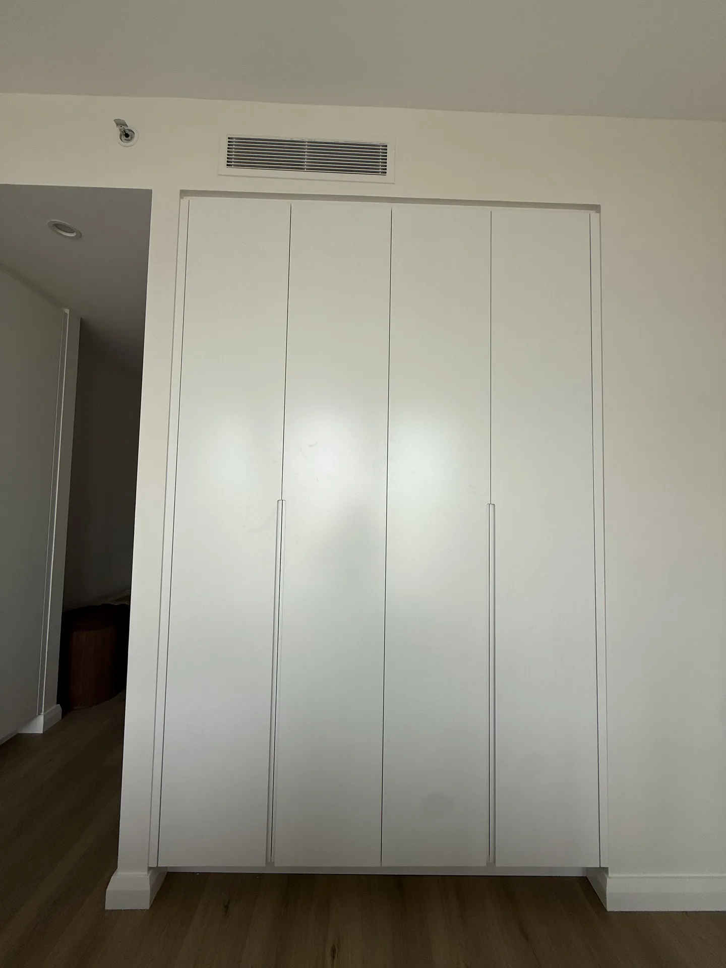 Floor-to-ceiling white wardrobe doors with slim vertical pulls beside a bedroom doorway